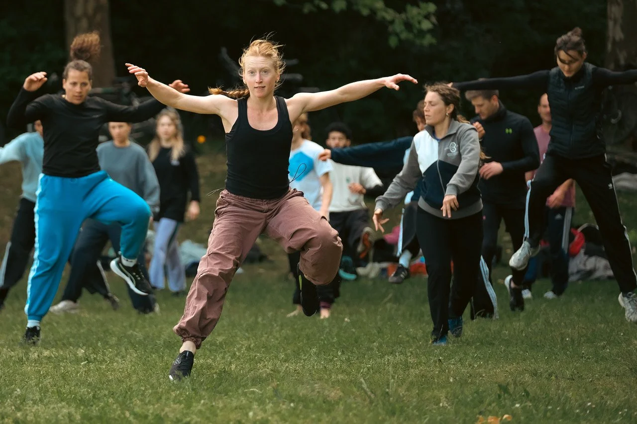Group of people practicing outdoor fitness exercises on a grassy field in a wooded area.