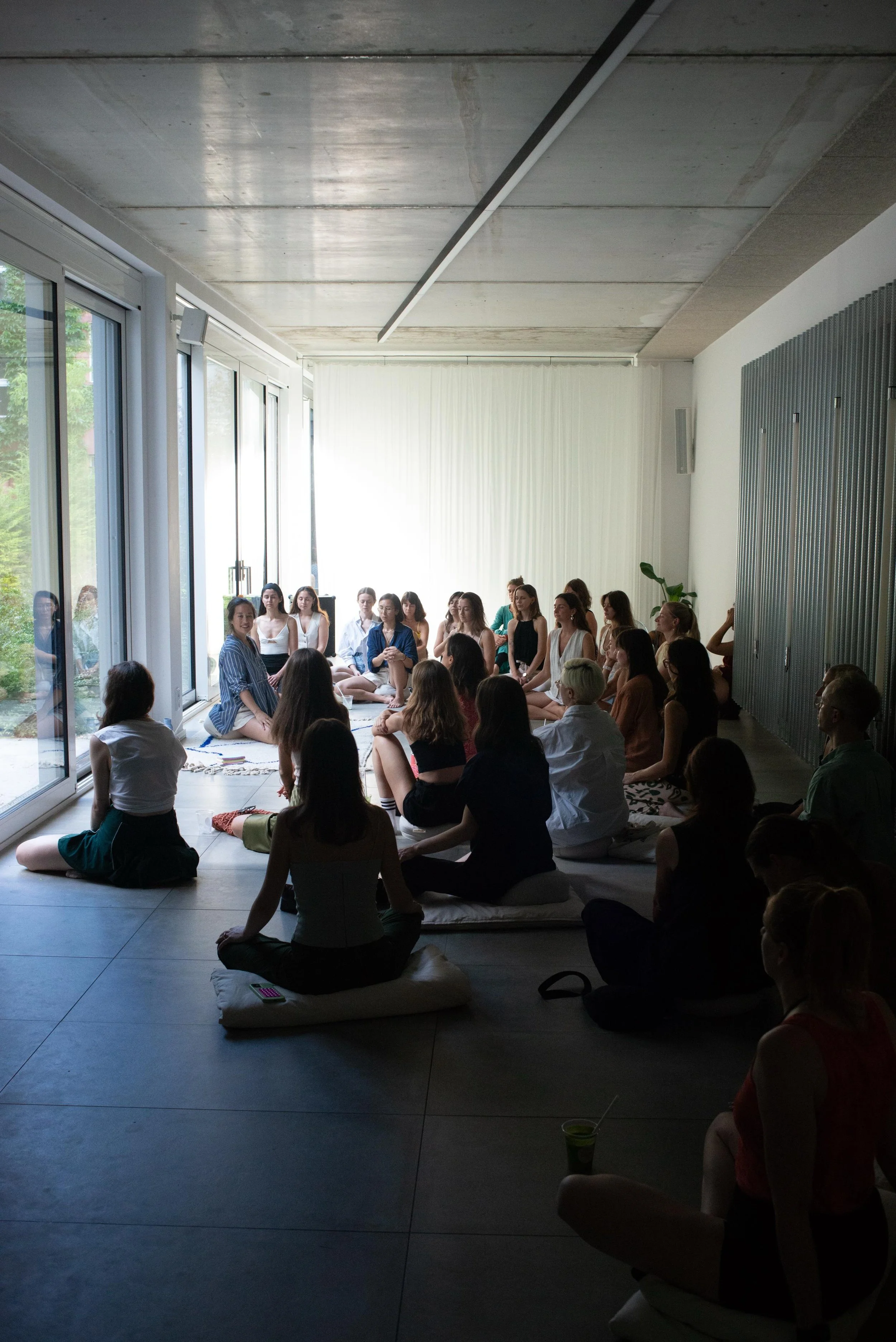 A group of people sitting on cushions and mats, attending a wellness community gathering sponsored by Squarespace in a bright, minimalist room with large windows and sliding glass doors.
