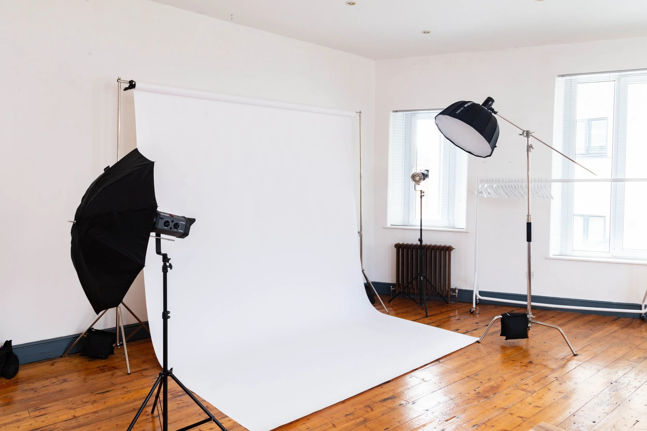Photography studio with white backdrop, lighting equipment, and a wooden floor.
