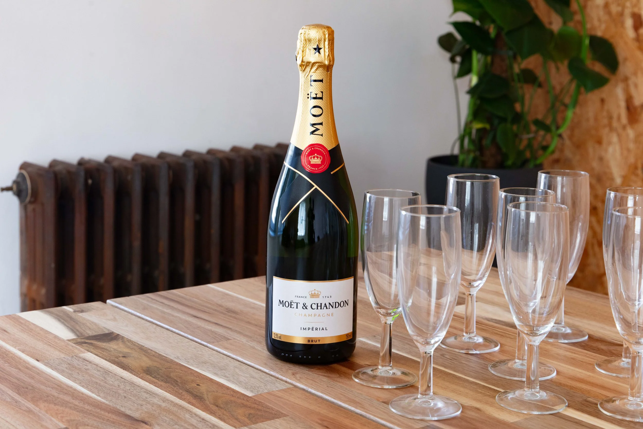 A bottle of Moët & Chandon champagne next to six empty champagne flutes on a wooden table
