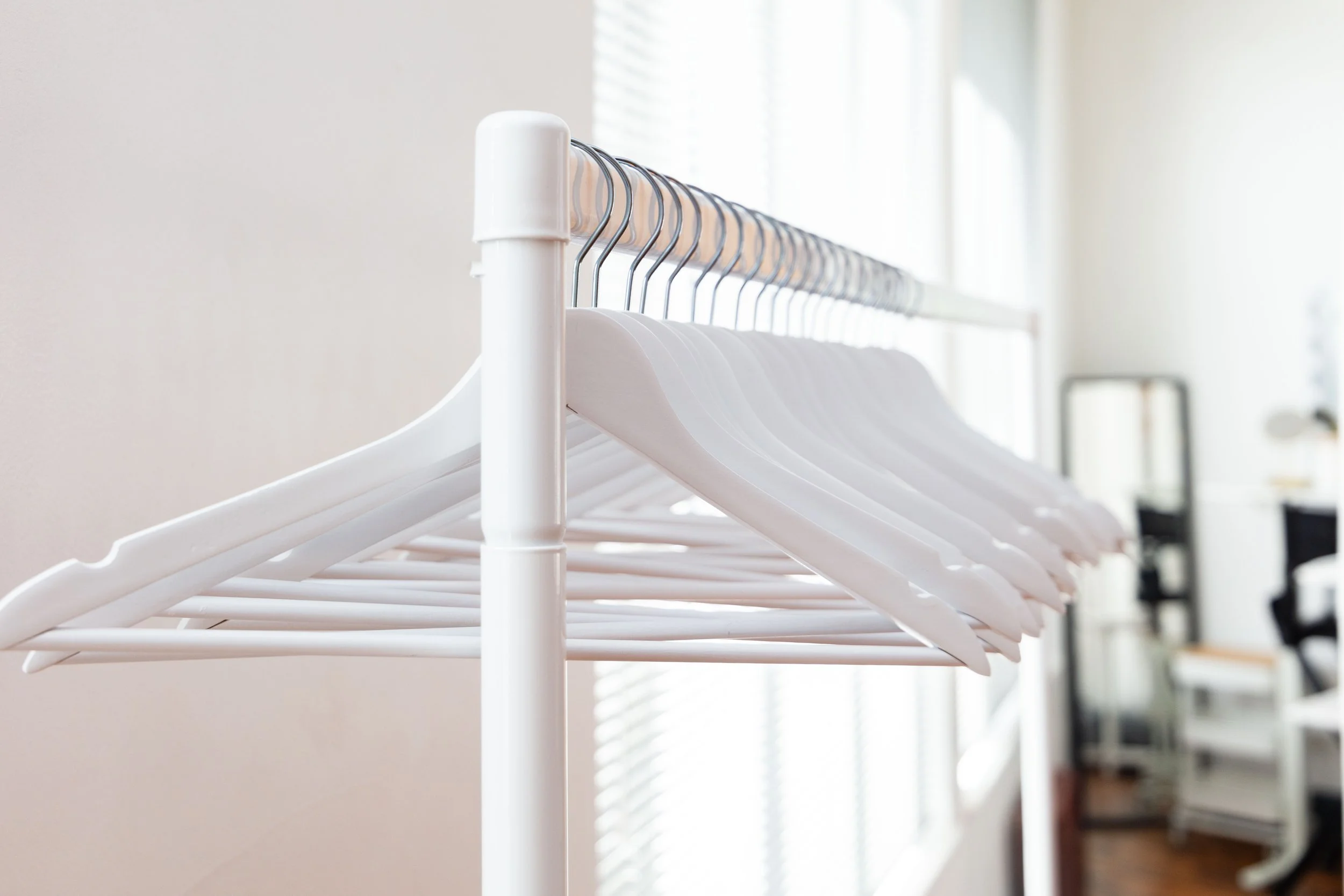 White empty clothes hangers on a white clothing rack in a well-lit room.