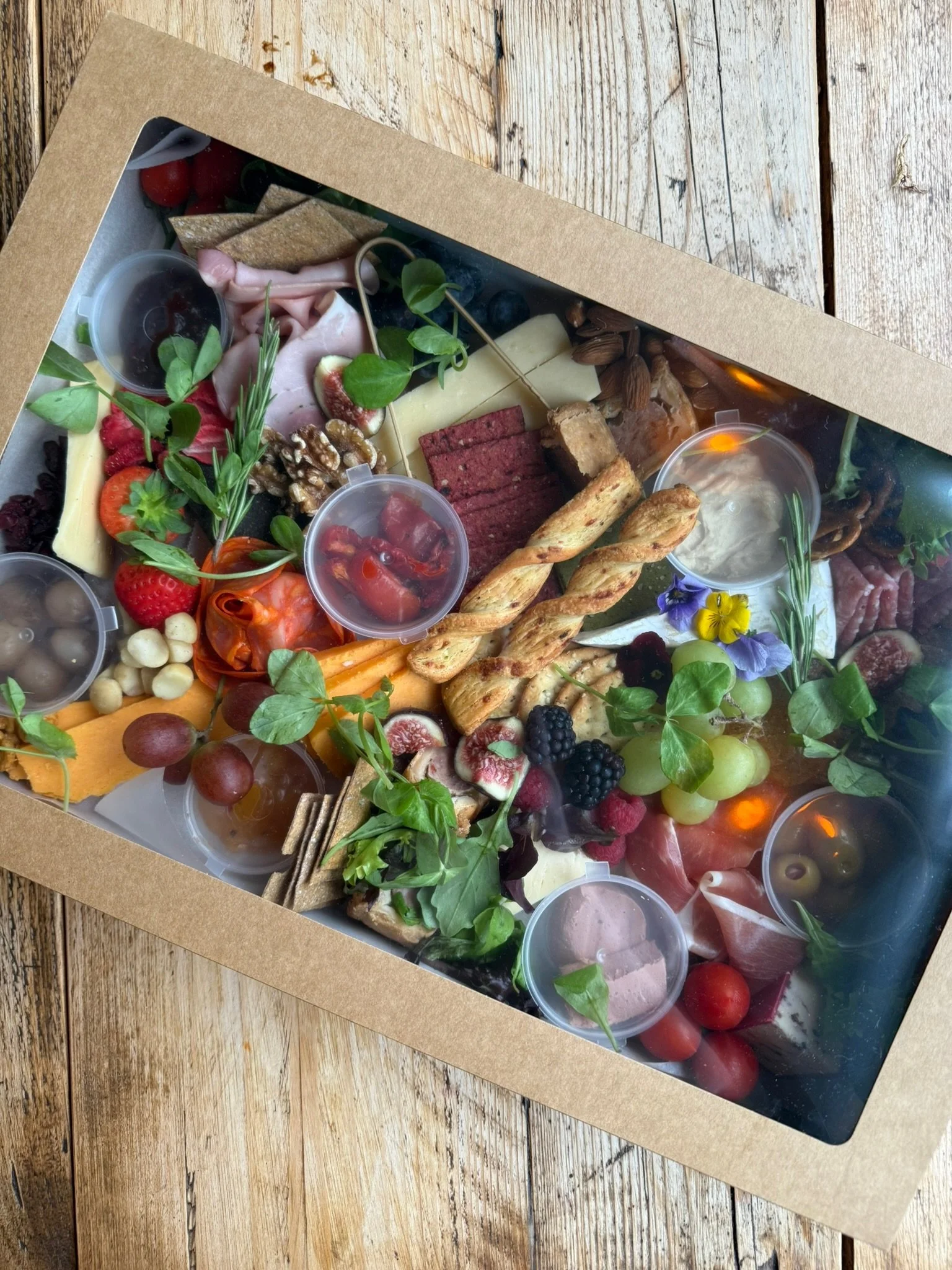 A charcuterie board with assorted cheeses, meats, fruits, nuts, crackers, breadsticks, and garnishes, arranged on a wooden surface.