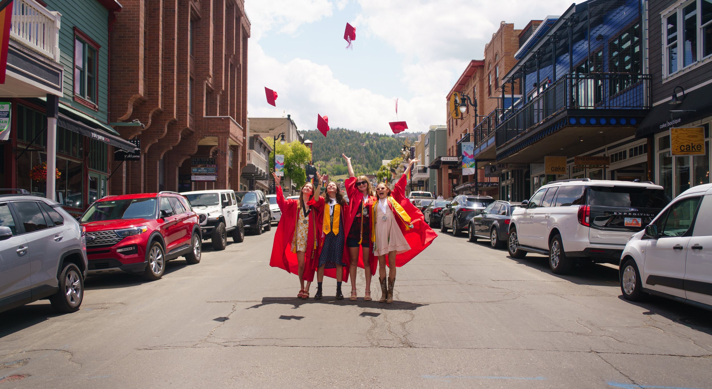 Group of young women in graduation gowns celebrating on a city street with flying graduation caps.