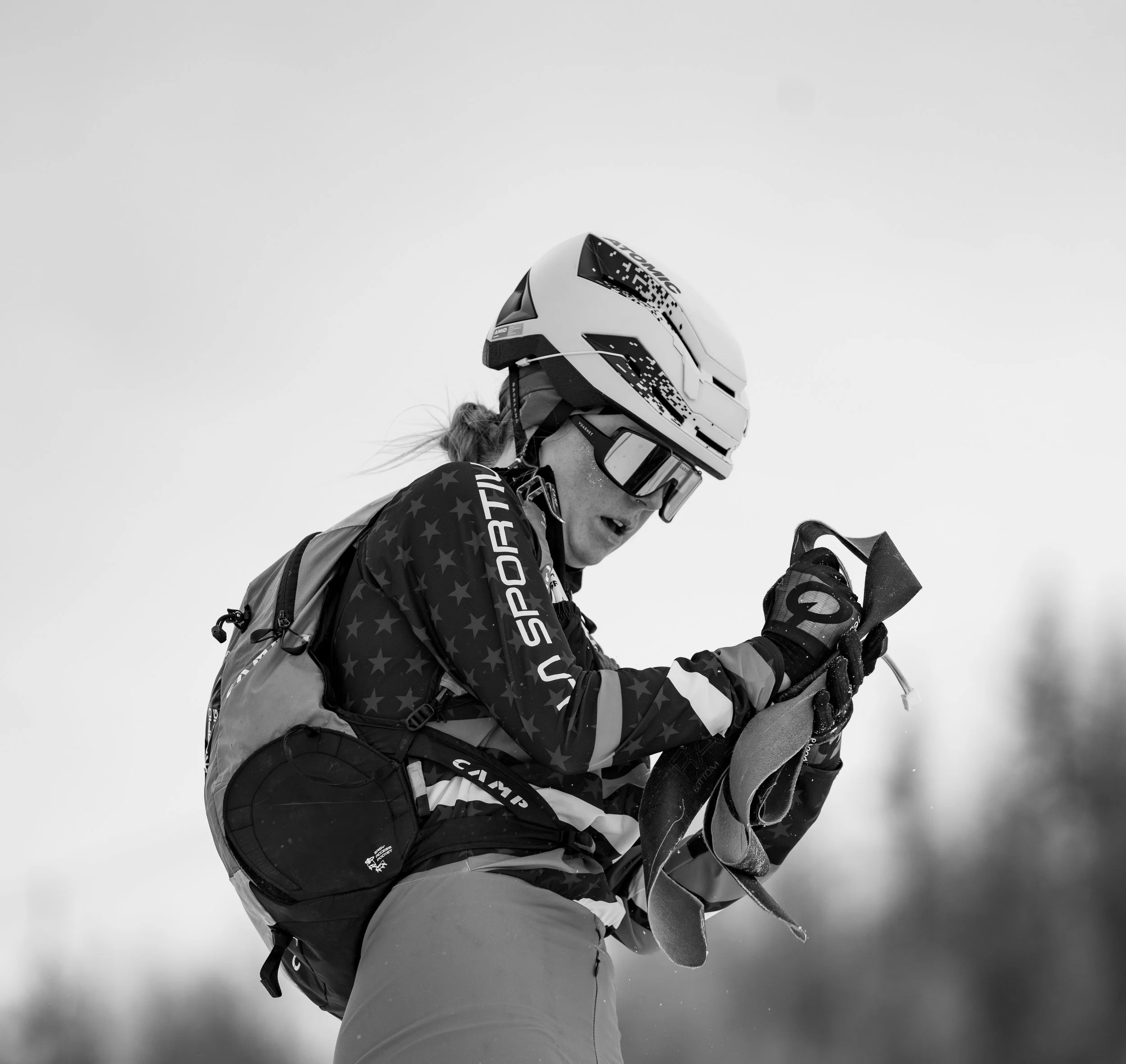 A person wearing a sports helmet, goggles, and a jacket with stars, holding ski poles, appears to be in a snowy environment, possibly preparing for or during skiing.