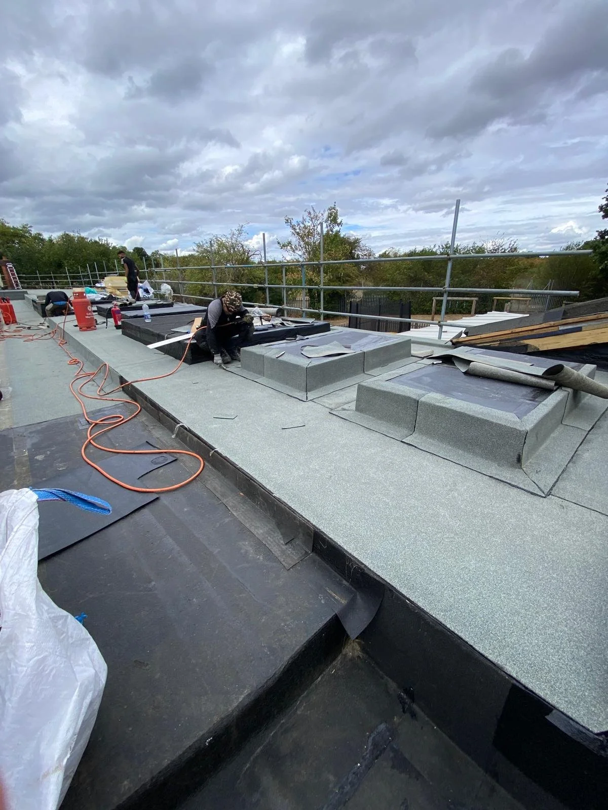 Construction workers installing a new roof on a building, with tools and materials scattered around, and a cloudy sky overhead.