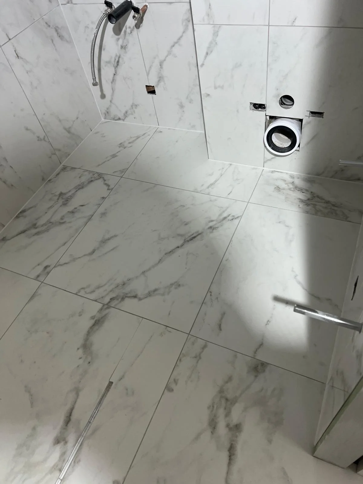 Bathroom with marble tiled floor and wall, with a wall-mounted showerhead, toilet pipe connection, and an open door.