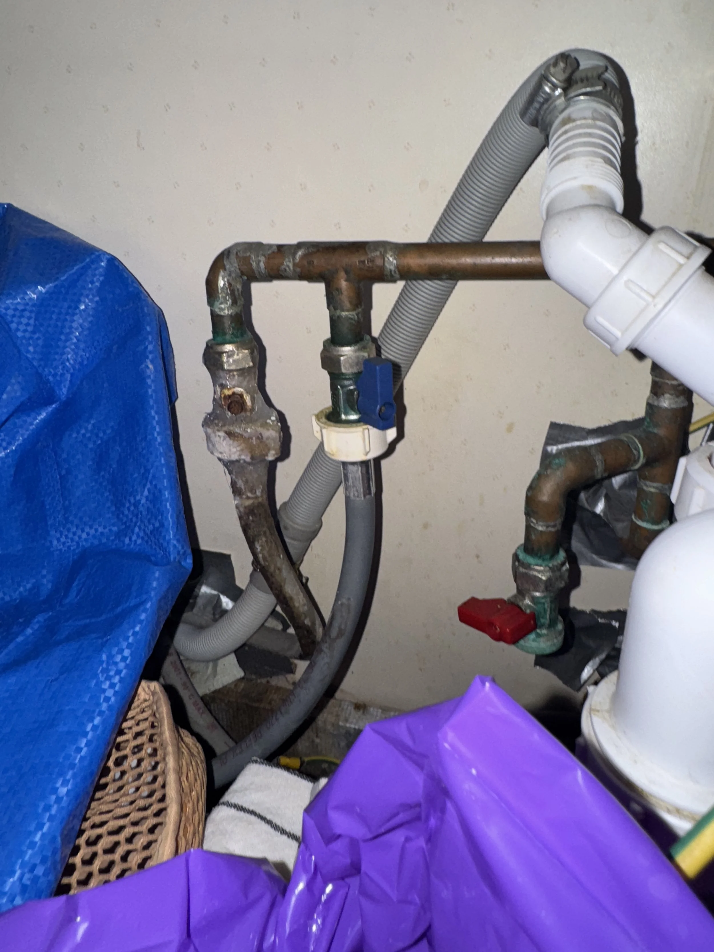 A close-up of plumbing pipes and fittings with a blue cover on the left and purple plastic objects in the foreground.