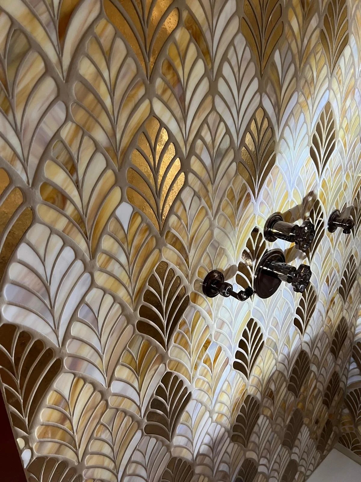 Close-up of a decorative wall with a black adjustable light fixture attached, featuring a pattern of leaf-like shapes in shades of cream, gold, and brown.