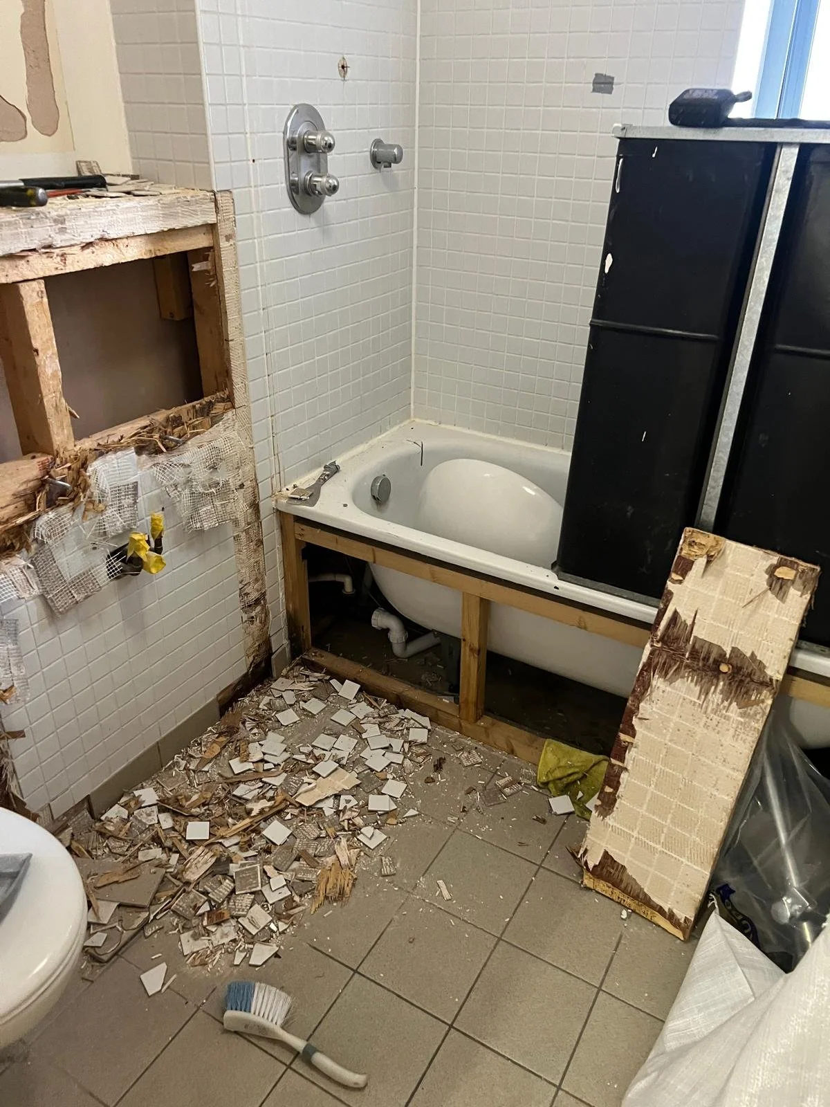 Bathroom under renovation with broken tile debris on the floor, an unfinished bathtub, a wooden frame, and construction tools.