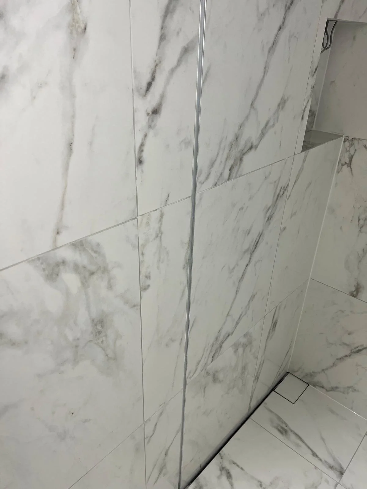 Close-up of a marble tiled shower wall with a built-in niche and a shower drain at the bottom.