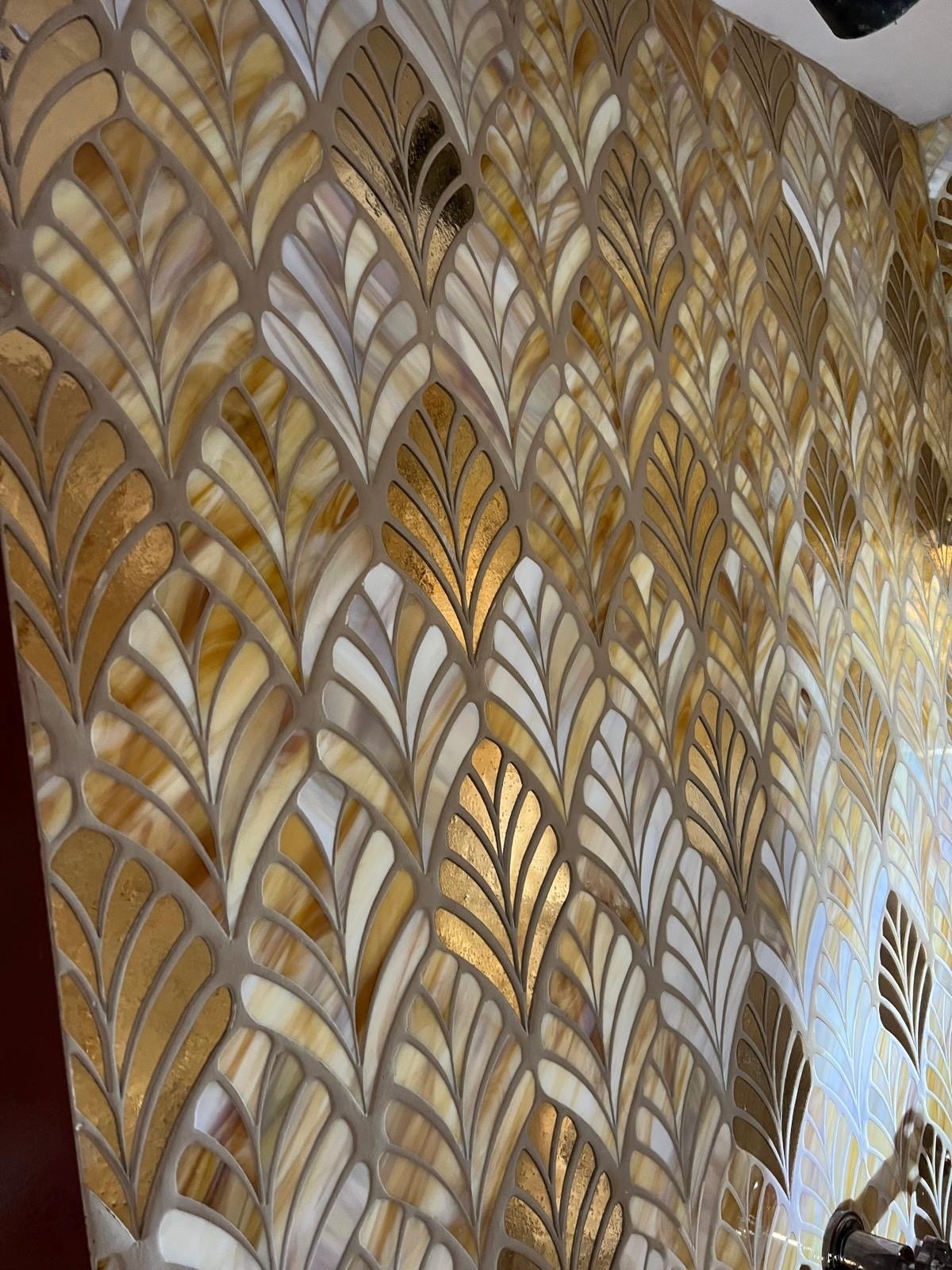 Close-up view of a decorative wall made of multiple onyx stone pieces arranged in a repeating leaf pattern with backlighting, highlighting the warm beige, gold, and white colors of the stones.