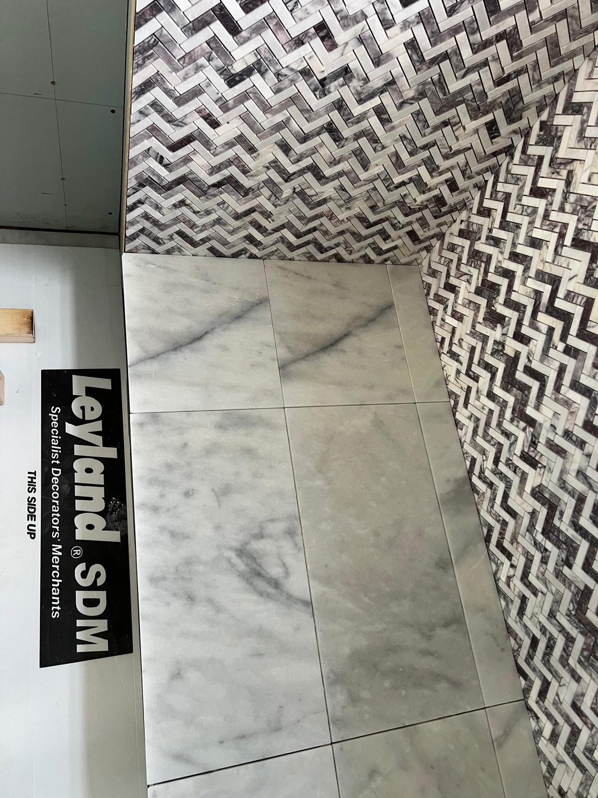 Display of various tiles, including large white marble tiles and a black and white herringbone pattern, with a Levi's label on the side.