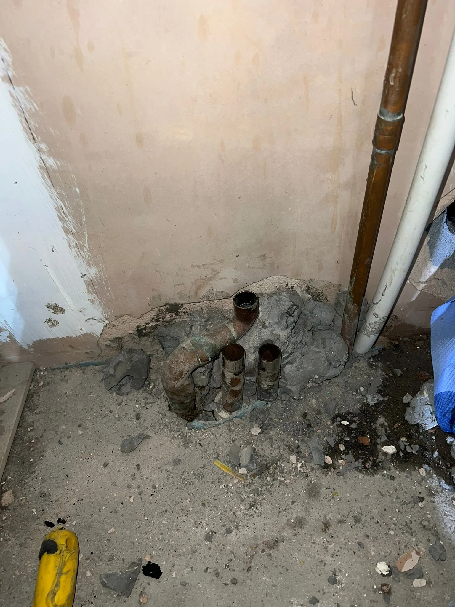 Construction site with exposed pipes and broken concrete on the floor.