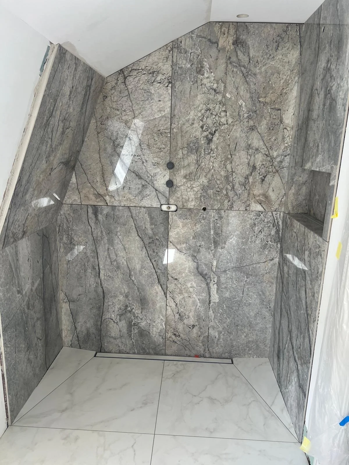 A shower with walls and a ceiling covered in gray veined marble tiles and a white floor with matching veined marble tiles.
