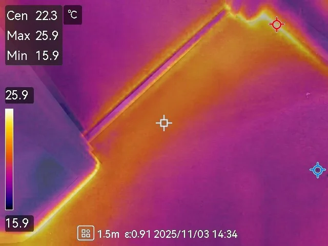 Thermal image showing a wall with a pipe or conduit running along it, with temperature readings indicating warmer and cooler areas.