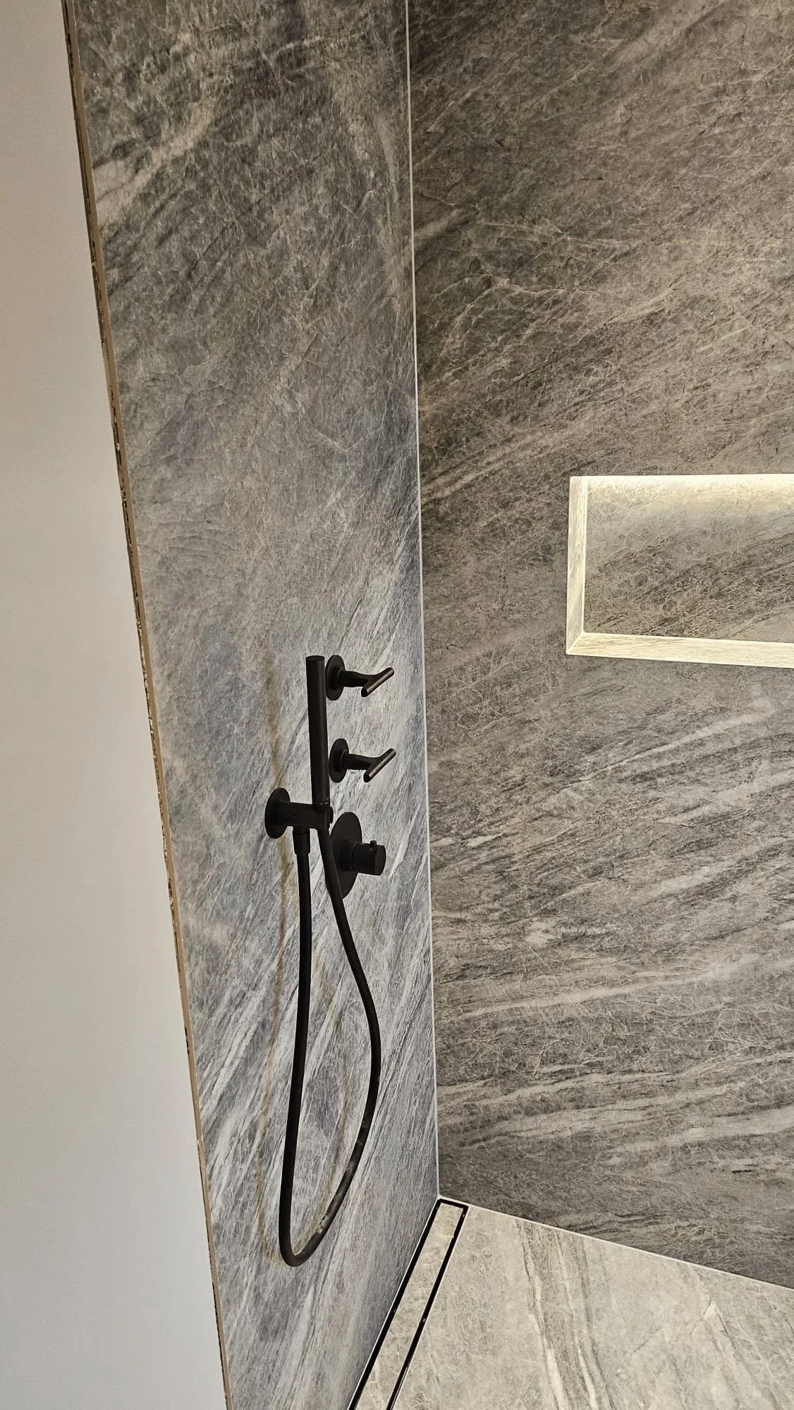 Modern shower with gray tiled wall, black shower fixtures, and a built-in recessed shower niche.