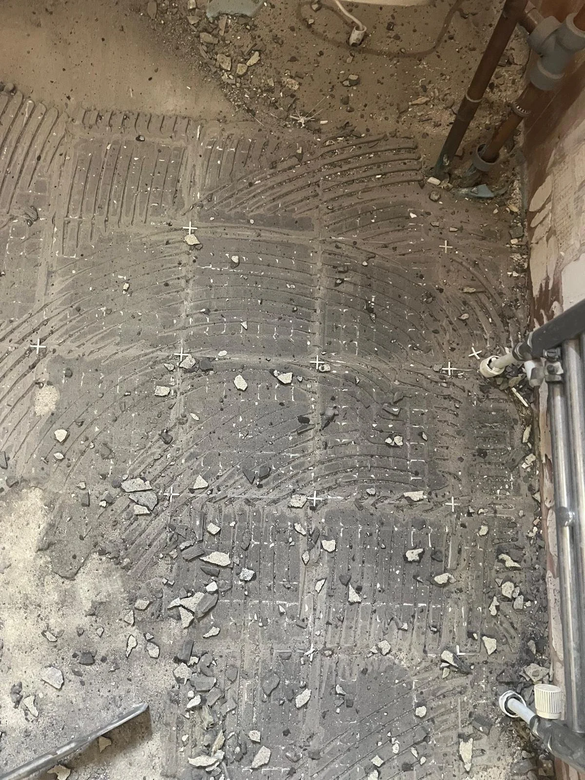 Subfloor with tile heating system installed, with heated cable grooves visible and some broken tiles and loose debris scattered on top.