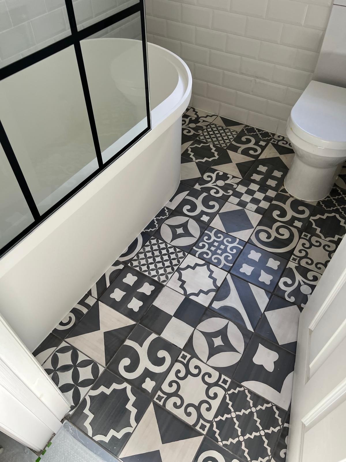 A bathroom with a bathtub, a toilet, and a tiled floor with black and white patterned tiles.