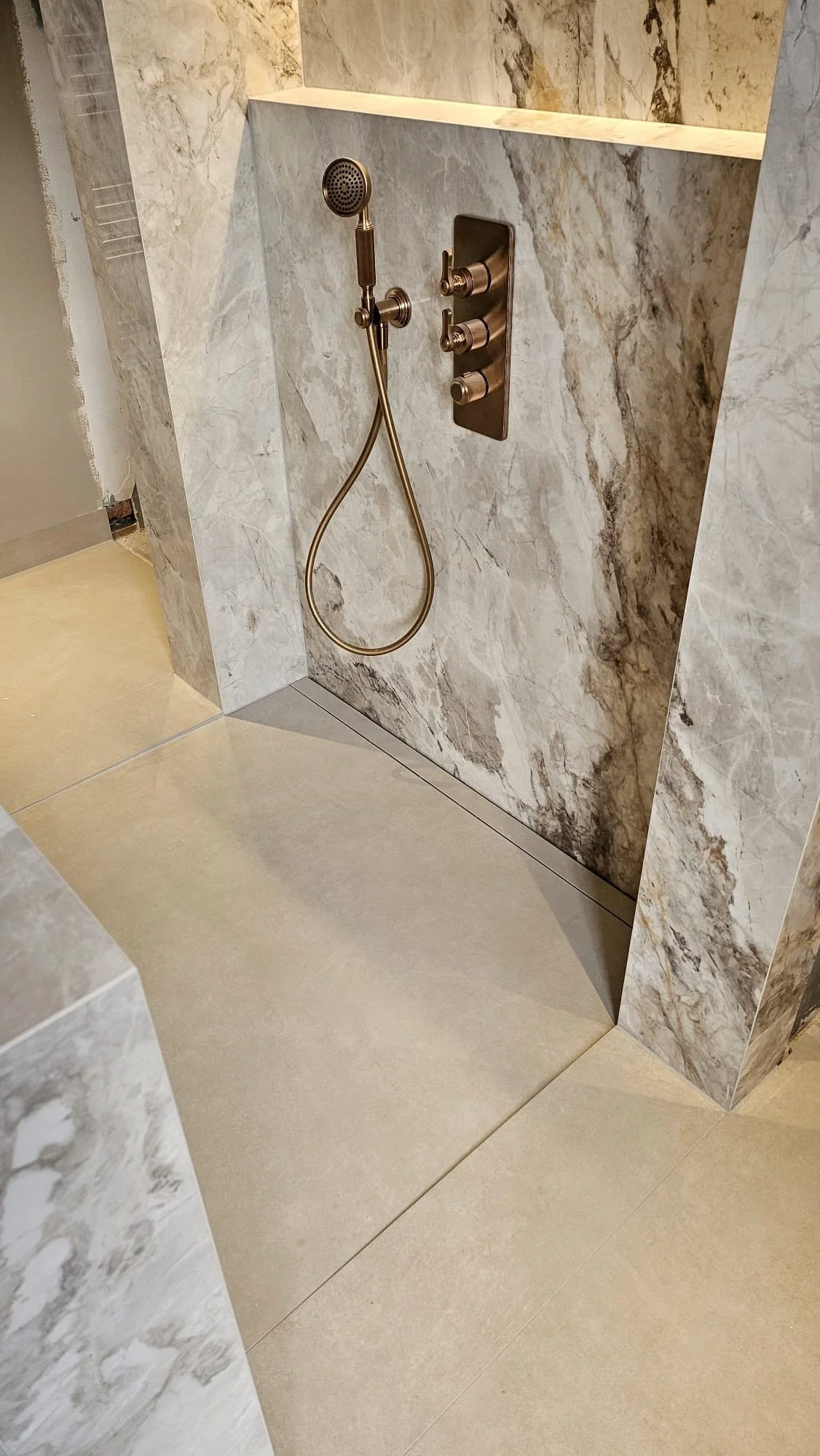 Modern shower area with marble walls, a handheld showerhead, and a control panel with three knobs.