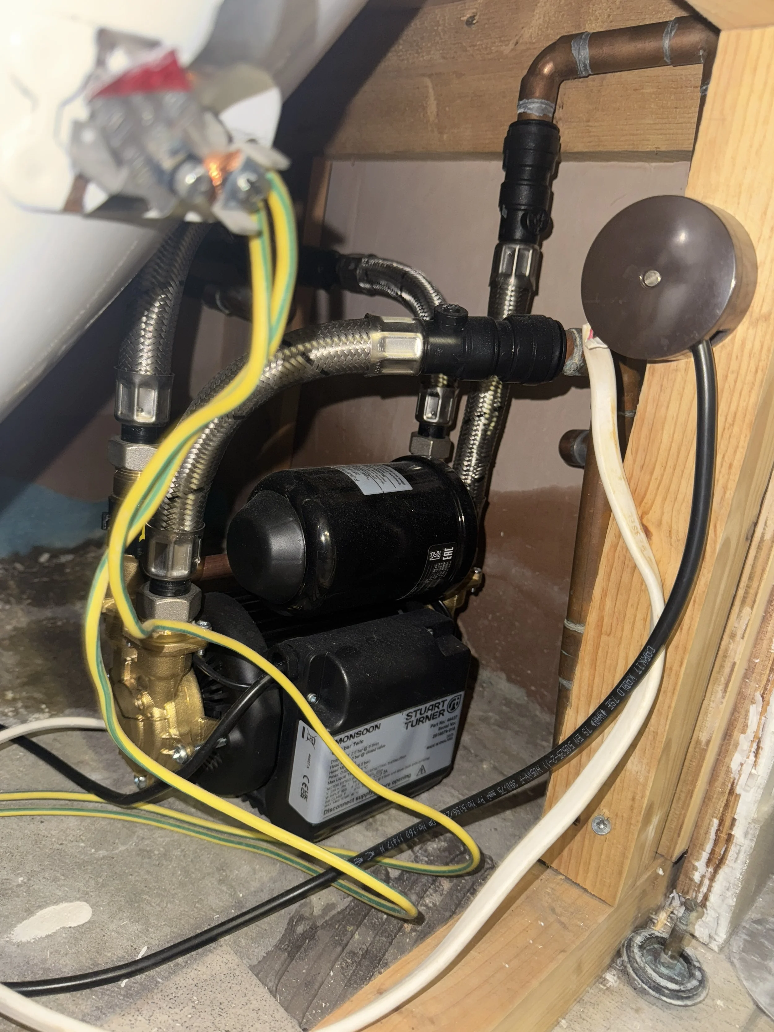 Various pipes, hoses, and a black water pump with a label, mounted on a wooden board in a plumbing installation.