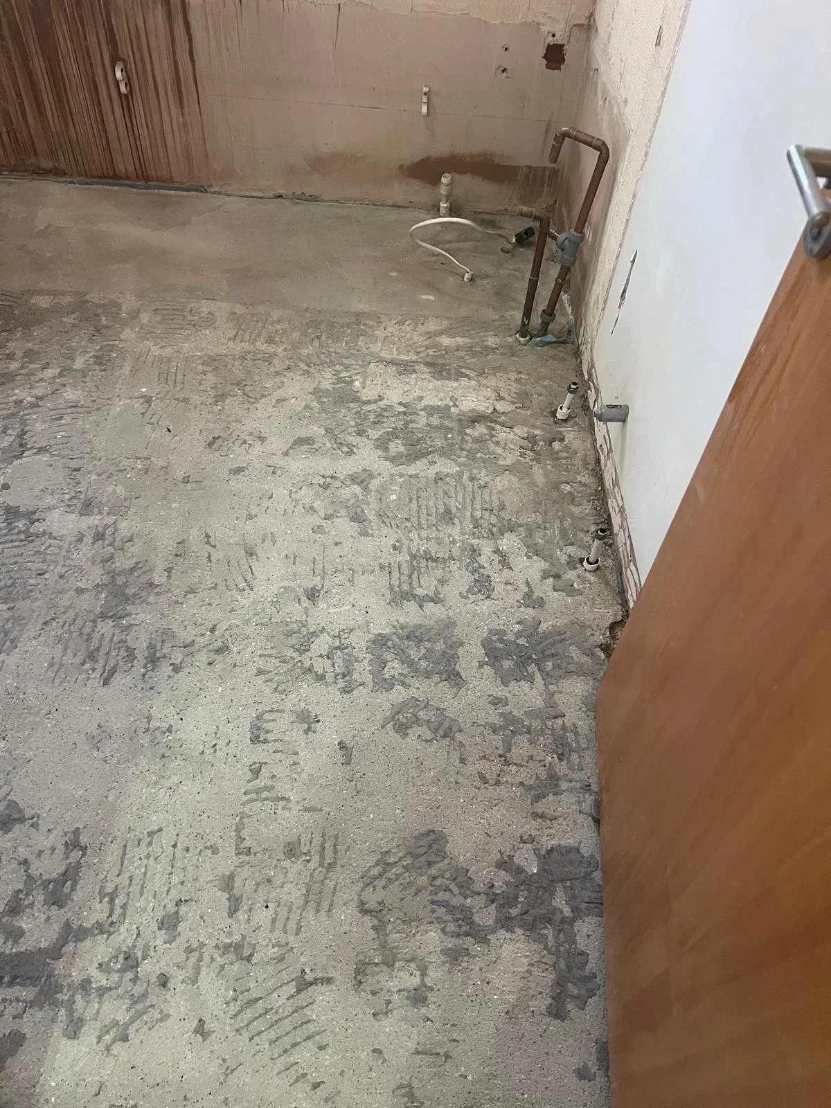 Construction area with exposed pipes and plumbing fixtures on a concrete floor and unfinished walls.