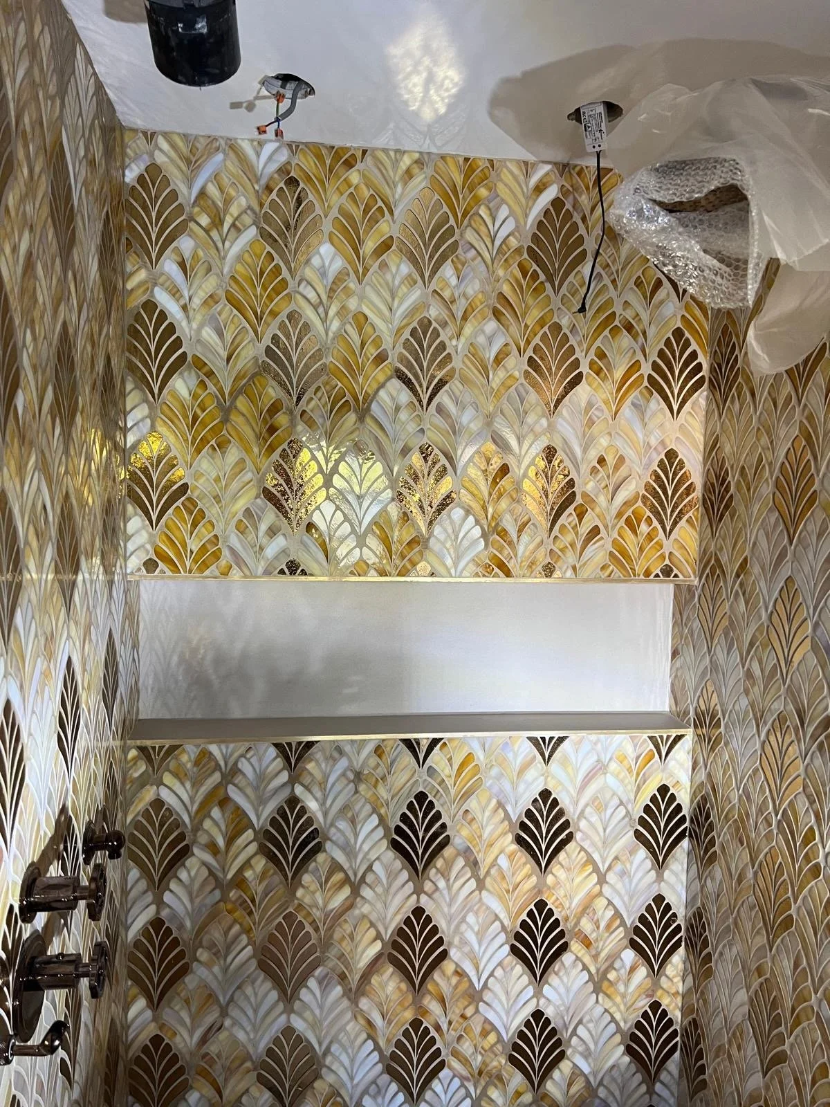 Interior of a bathroom with partly installed lighting fixtures and intricate gold and white patterned wallpaper.
