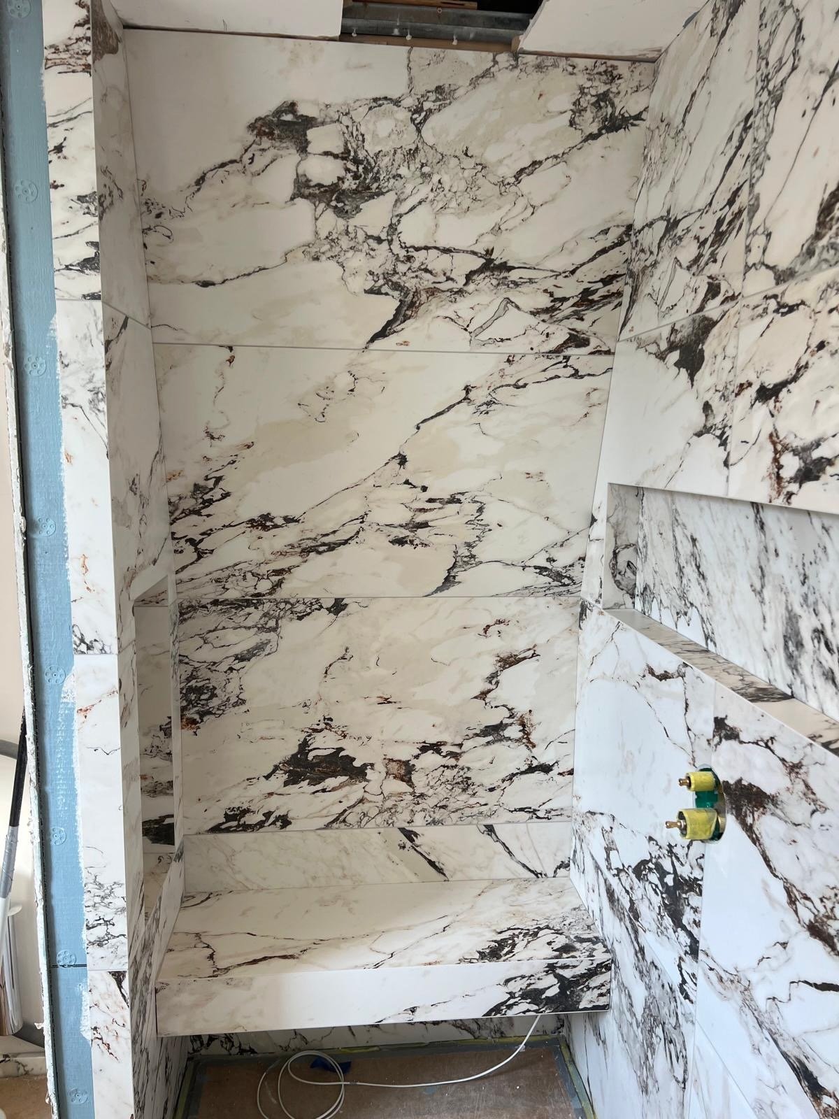 Interior view of a shower space with walls and floor covered in white marble tiles with black and dark brown veining.