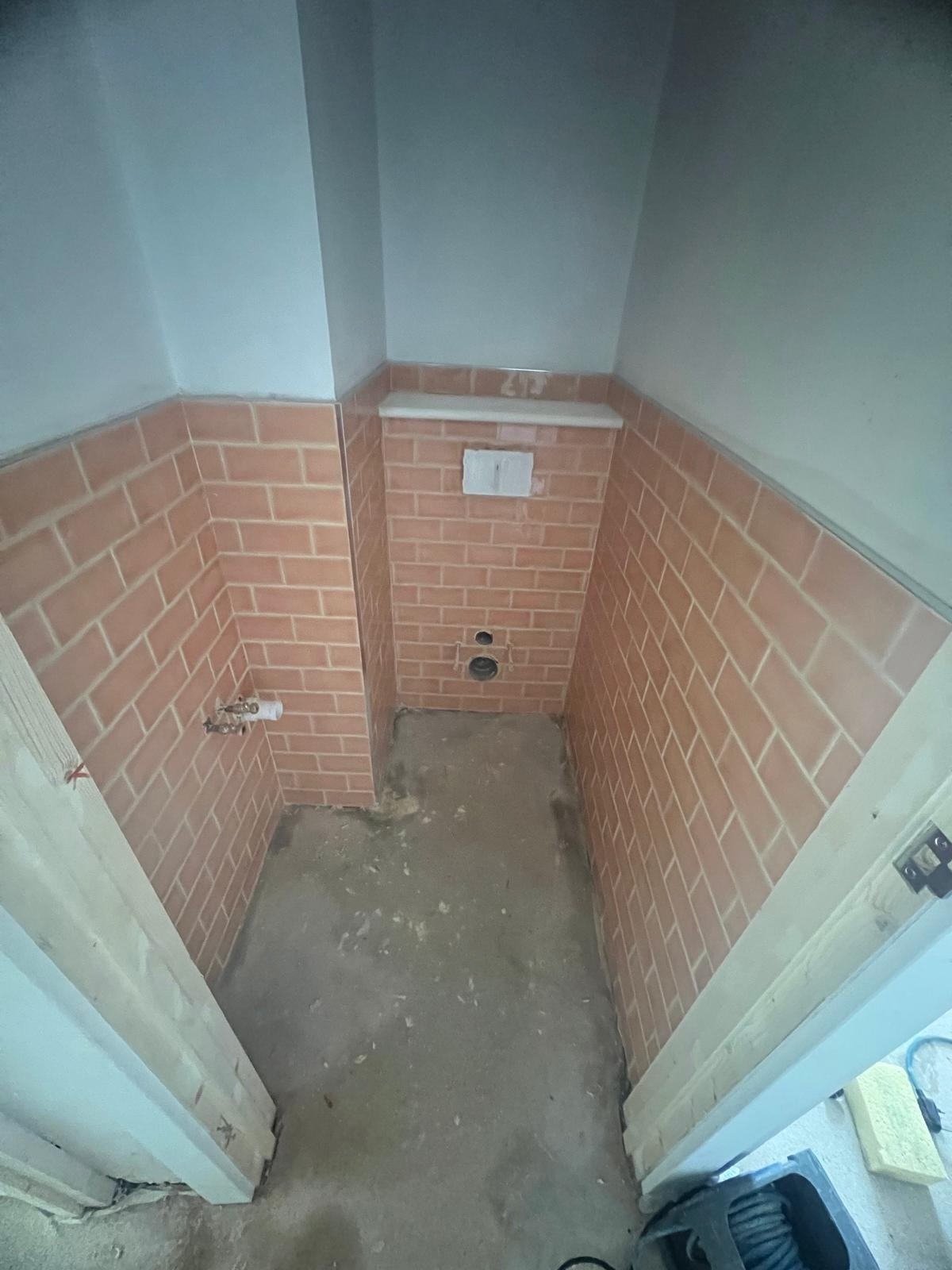 Empty bathroom with brick walls, a small ledge, and plumbing fixtures, floor appears unfinished.