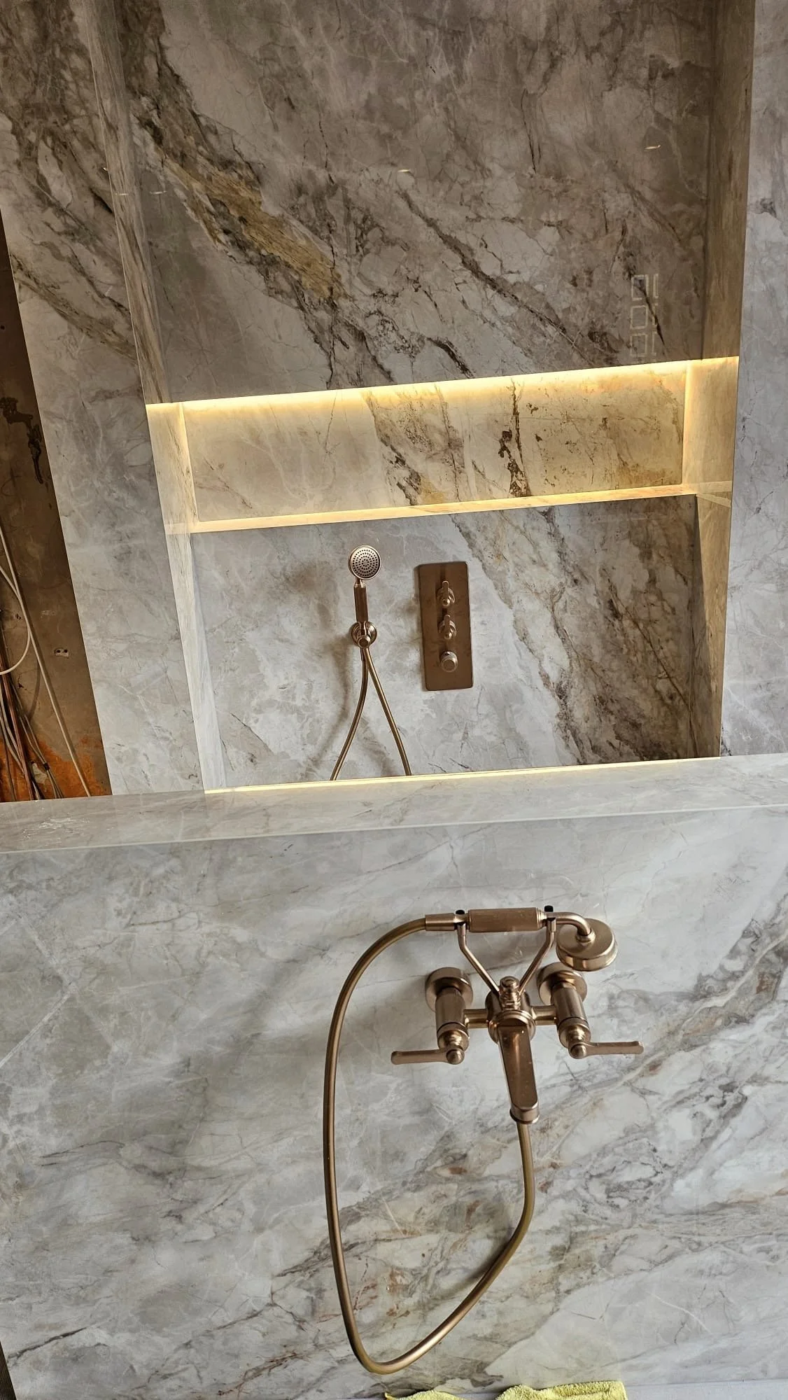 Marble shower with a handheld showerhead and built-in shelves lit with LED lighting.