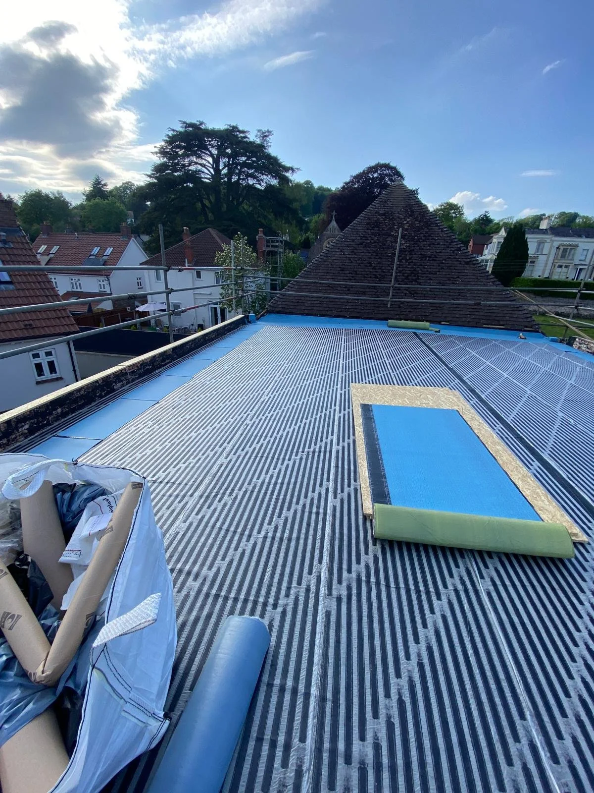 Roof under construction with solar panels installed, surrounding houses, trees, and a partly cloudy sky.