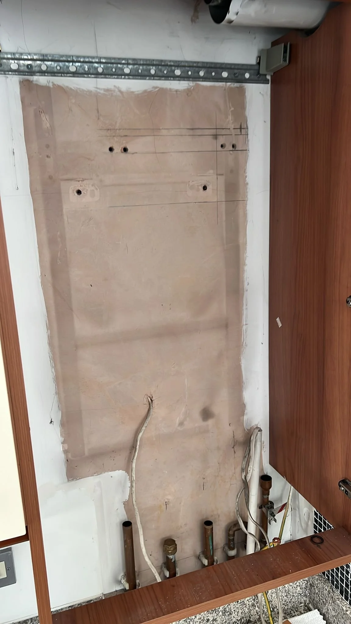 View of a kitchen wall with plumbing pipes, no cabinets or appliances installed yet, and a wooden countertop in the foreground.