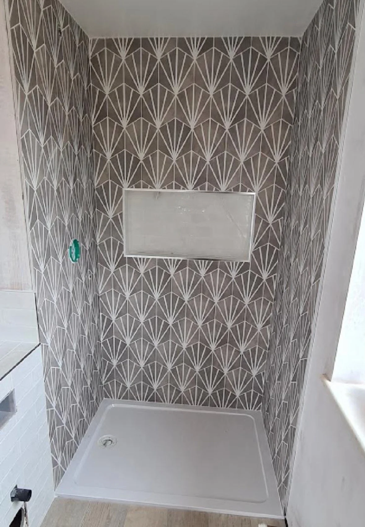 Bathroom shower area with geometric patterned tiles on the walls, a small window or mirror, and a white shower tray.