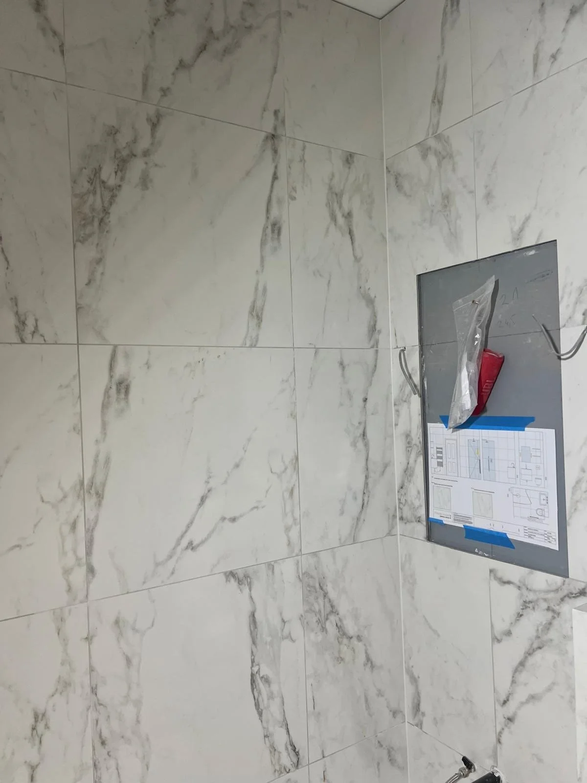 Marble wall tiles with installation instructions and tools attached to the wall, indicating ongoing construction or renovation.