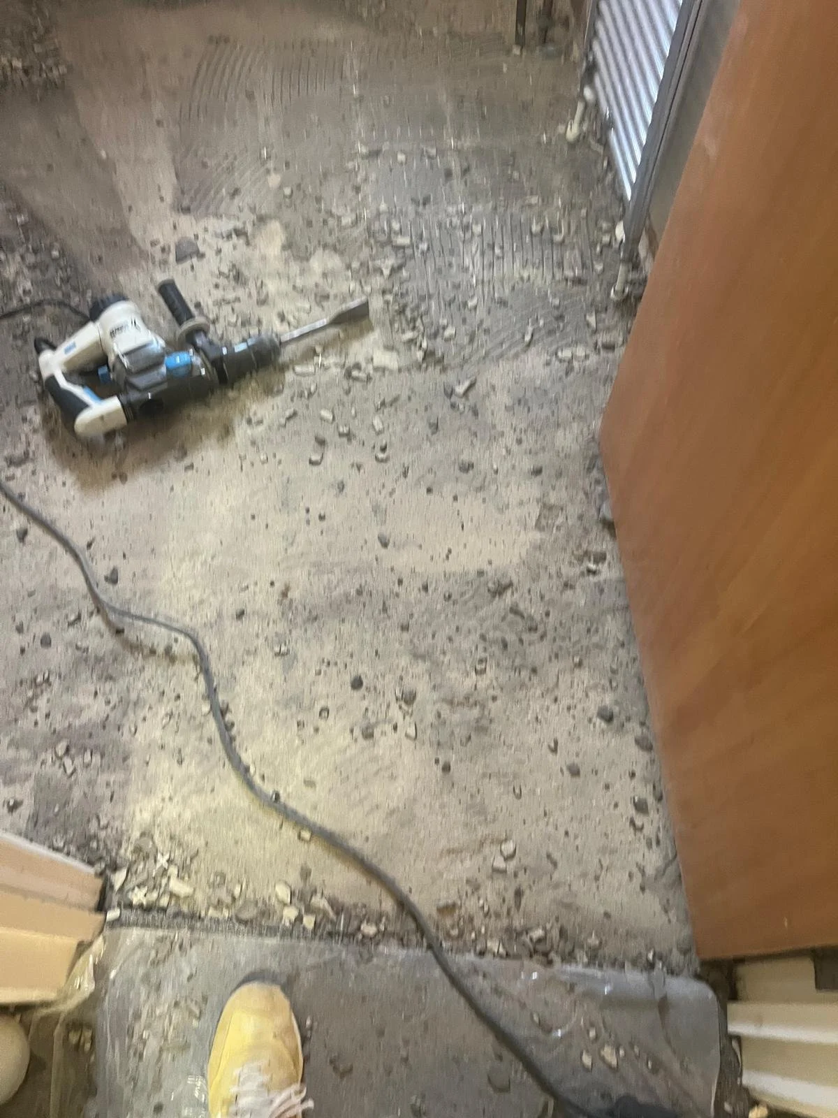 A wet concrete floor with scattered debris, a power tool, and a person wearing yellow shoes.