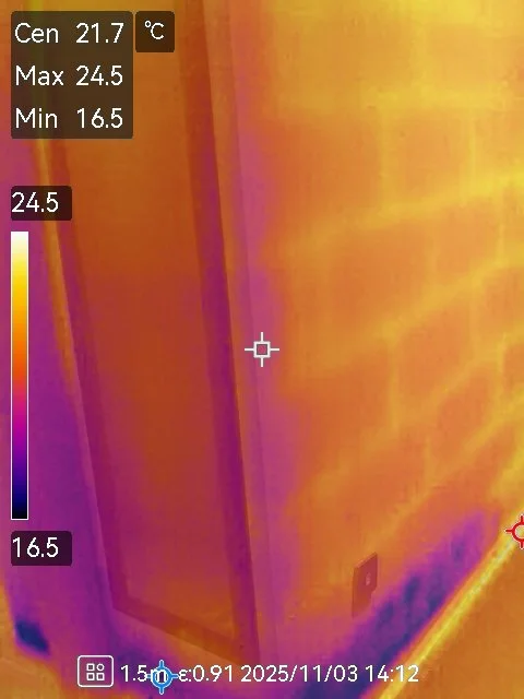 Infrared thermal image of a corner of a room showing temperature readings, with warm colors indicating higher temperatures and cooler colors indicating lower temperatures.