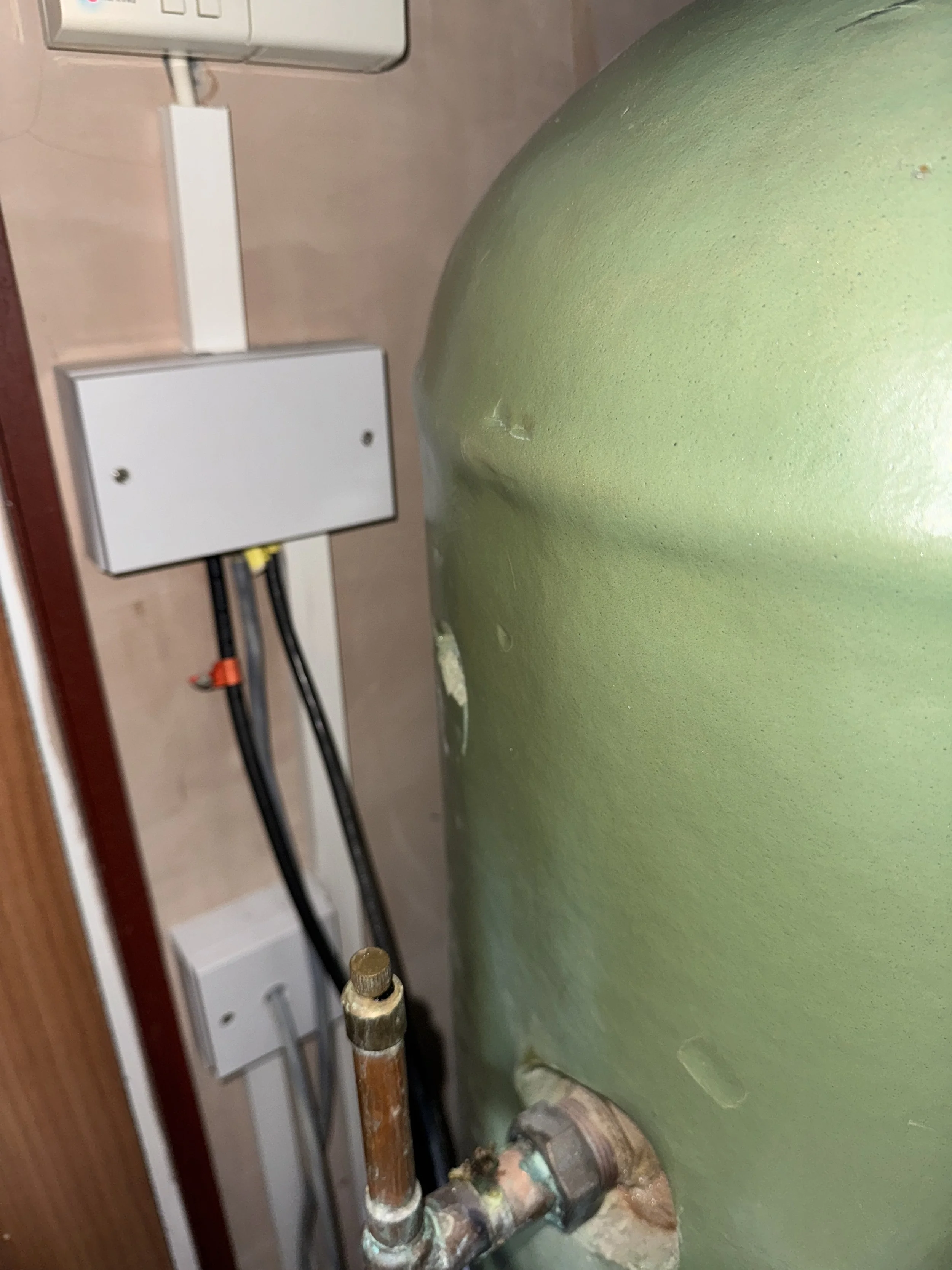 Close-up of pipes and electrical box mounted on a wall, next to a large green tank with water droplets.