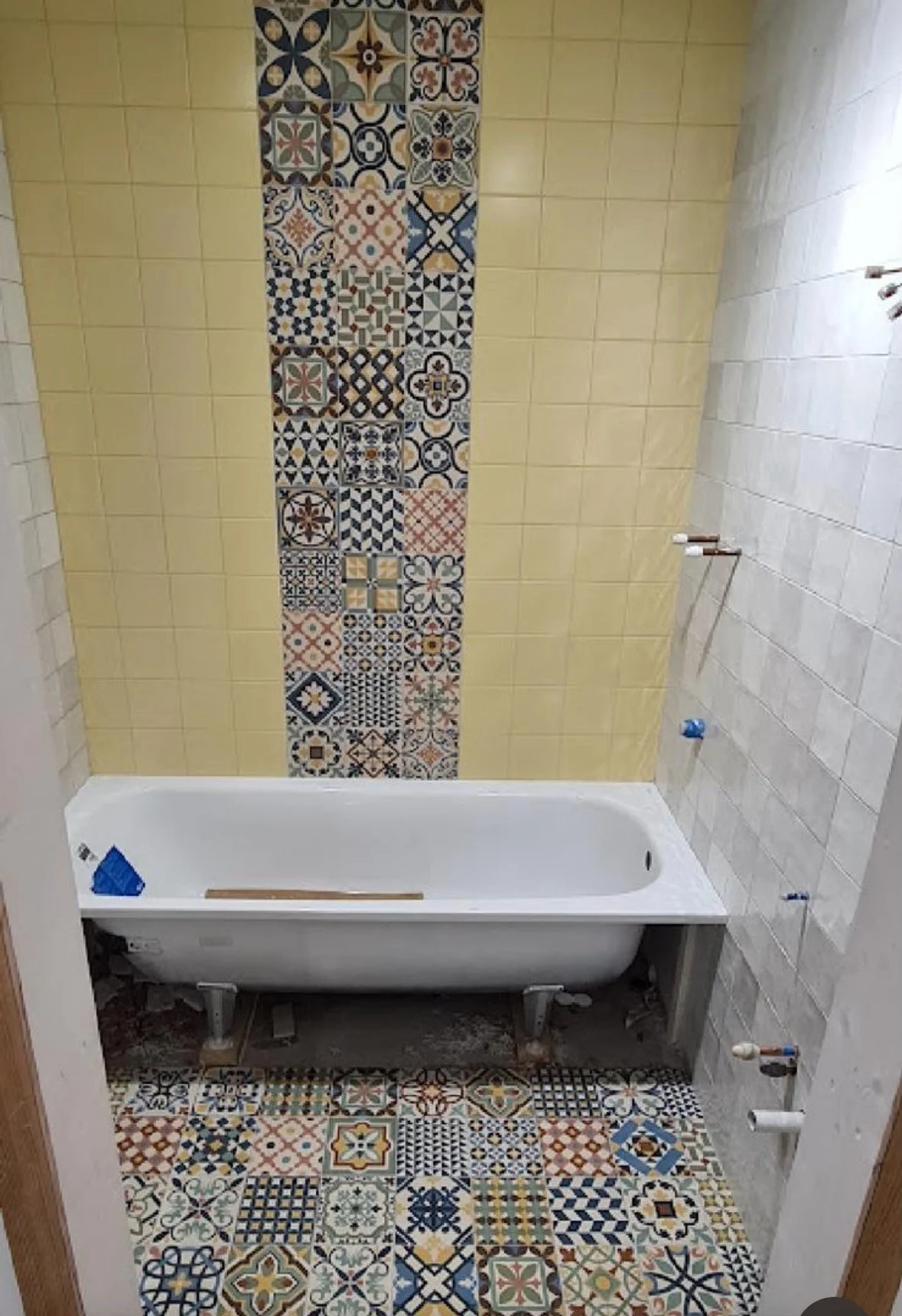 Bathroom with decorative patterned tiles on the wall, floor, and partially on the wall behind a bathtub under construction.