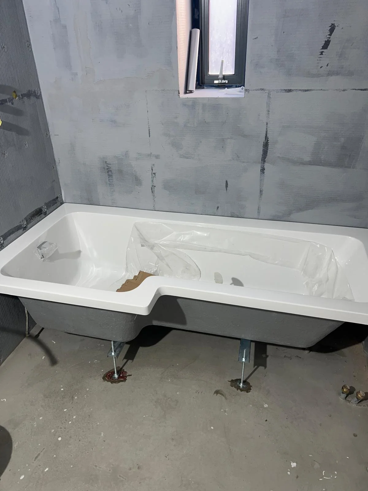 A bathroom under construction with a partially installed bathtub and unfinished wall drywall.