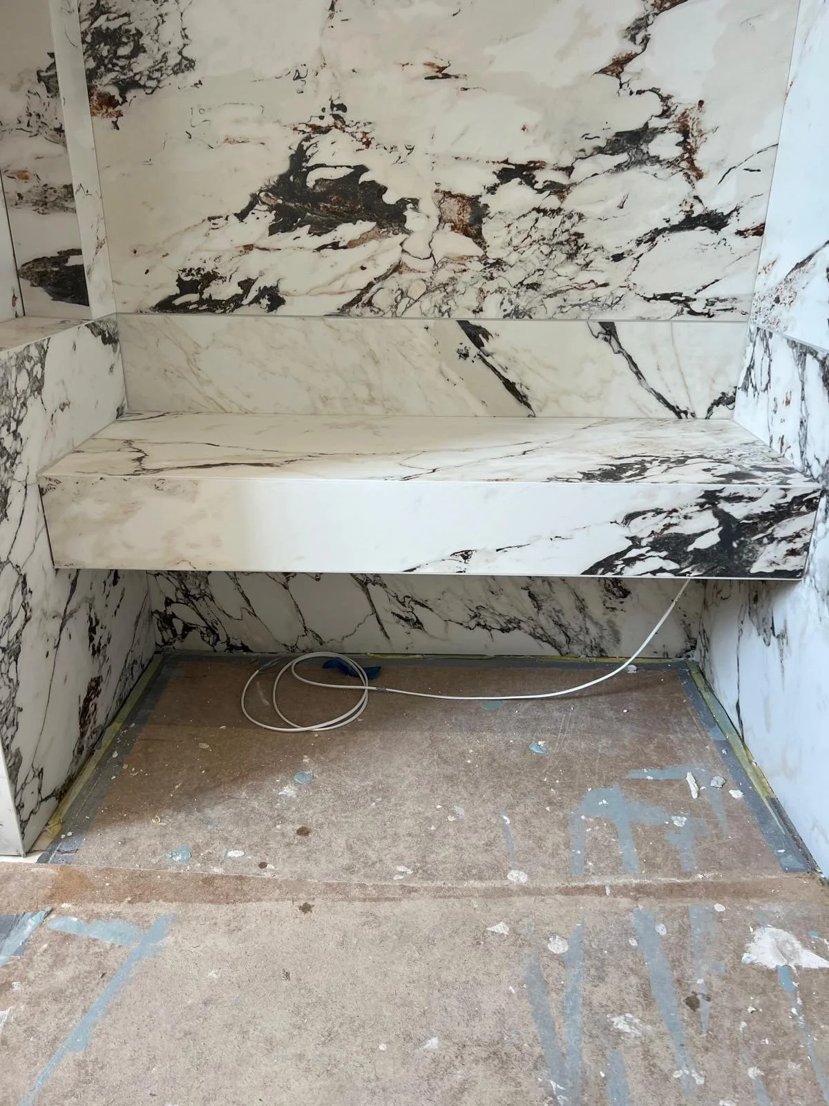 Marble wall and ledge with electrical cords on a construction floor.