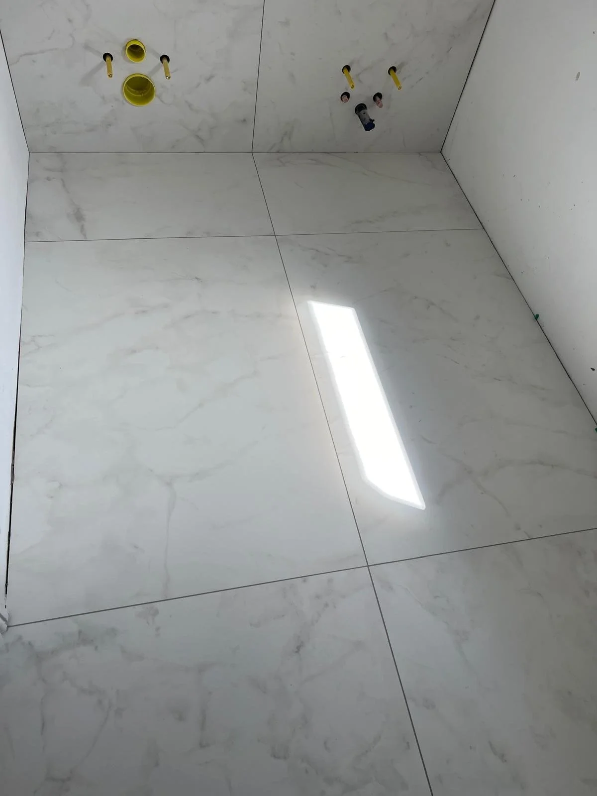Photograph of a tiled bathroom or laundry room ceiling with two plumbing pipes and a light reflection on the tiles.