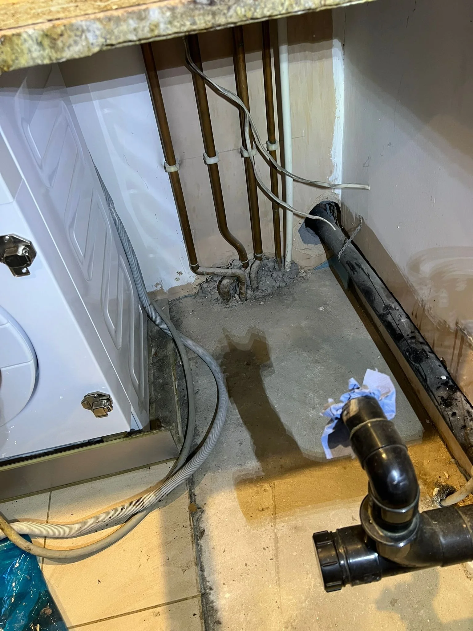 Pipes and tubes under a kitchen or laundry sink with a washing machine, showing plumbing work in progress.