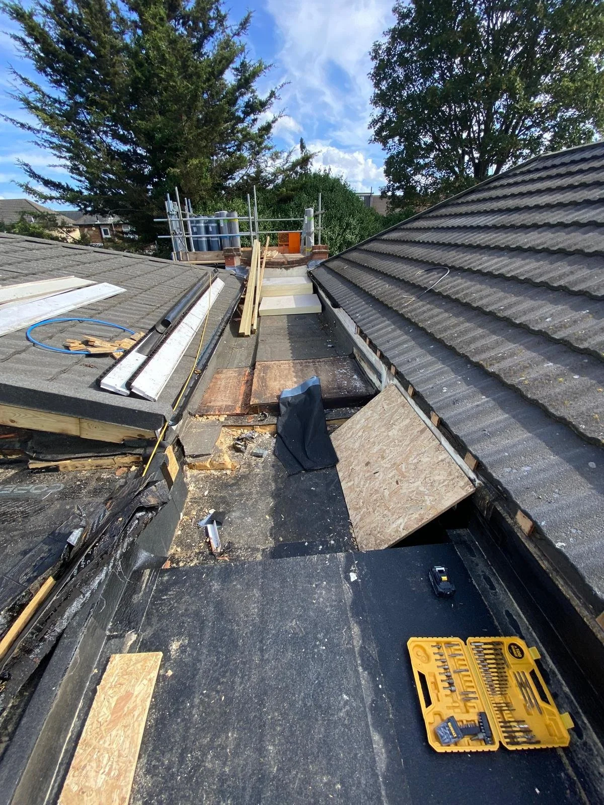Rooftop construction with wooden planks, tools, and roofing materials under a partly cloudy sky.