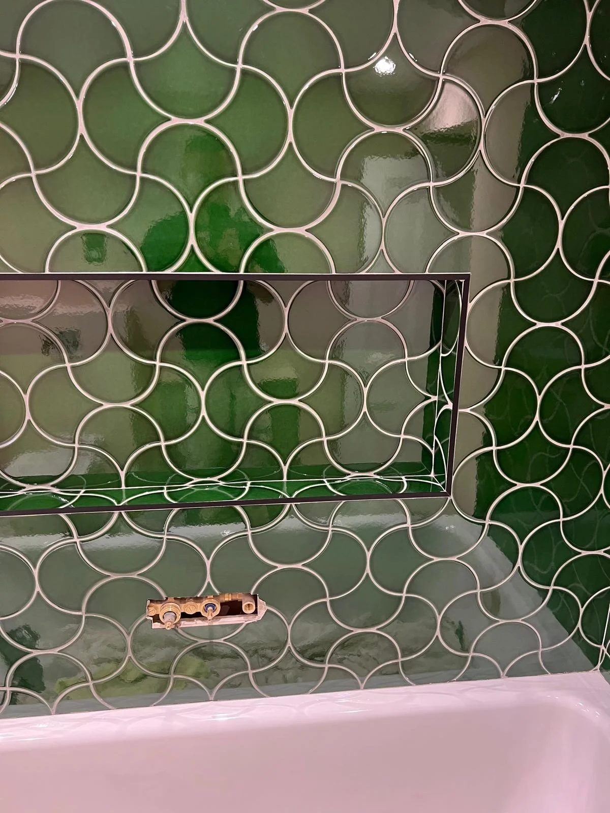 Green and white patterned tiled wall with a cutout in the center and a partially visible fixture at the bottom.