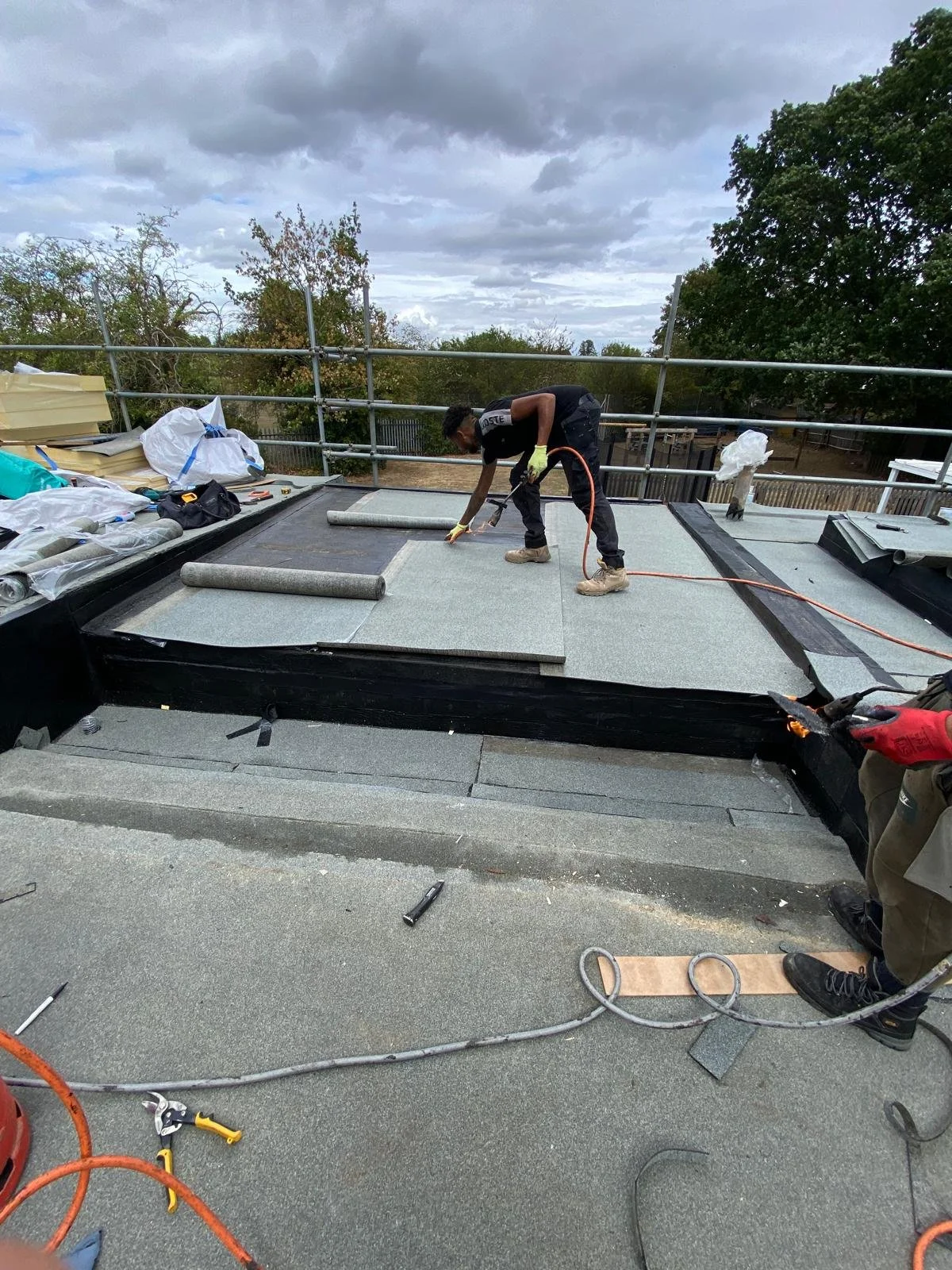 Construction workers installing roofing material on a building under a cloudy sky.