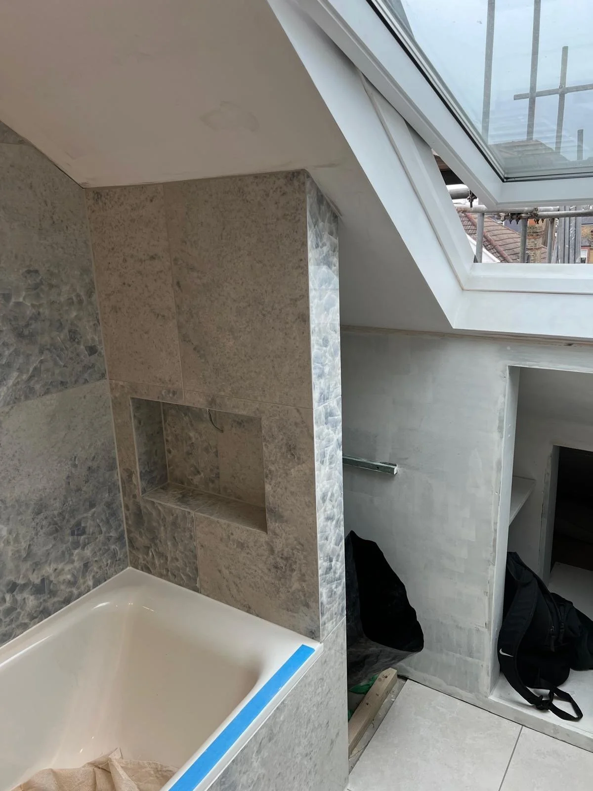 Bathroom under construction with a bathtub, tiled wall, and a skylight window in the ceiling.