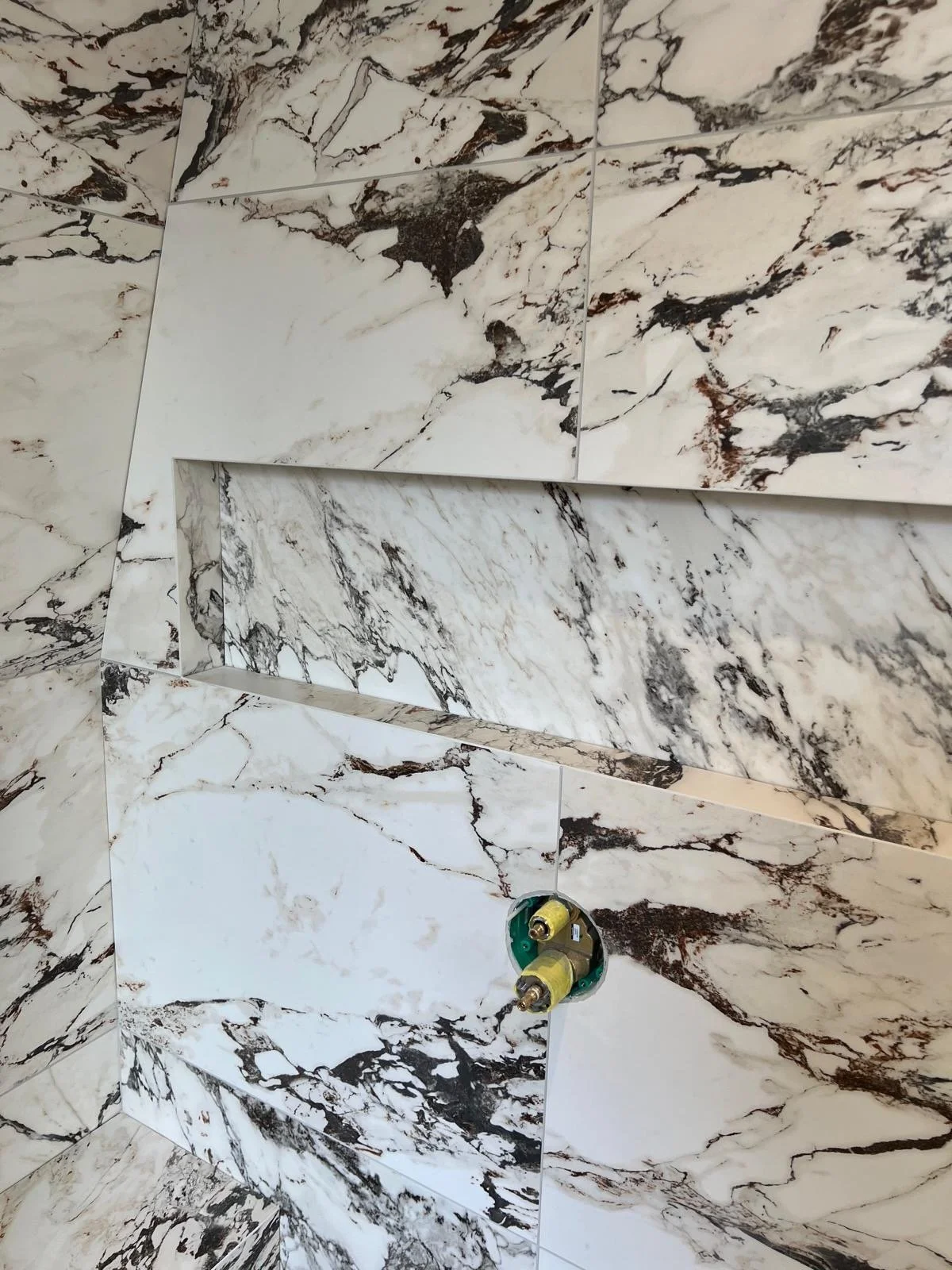 Marble tile wall with an opening and exposed plumbing fixtures.