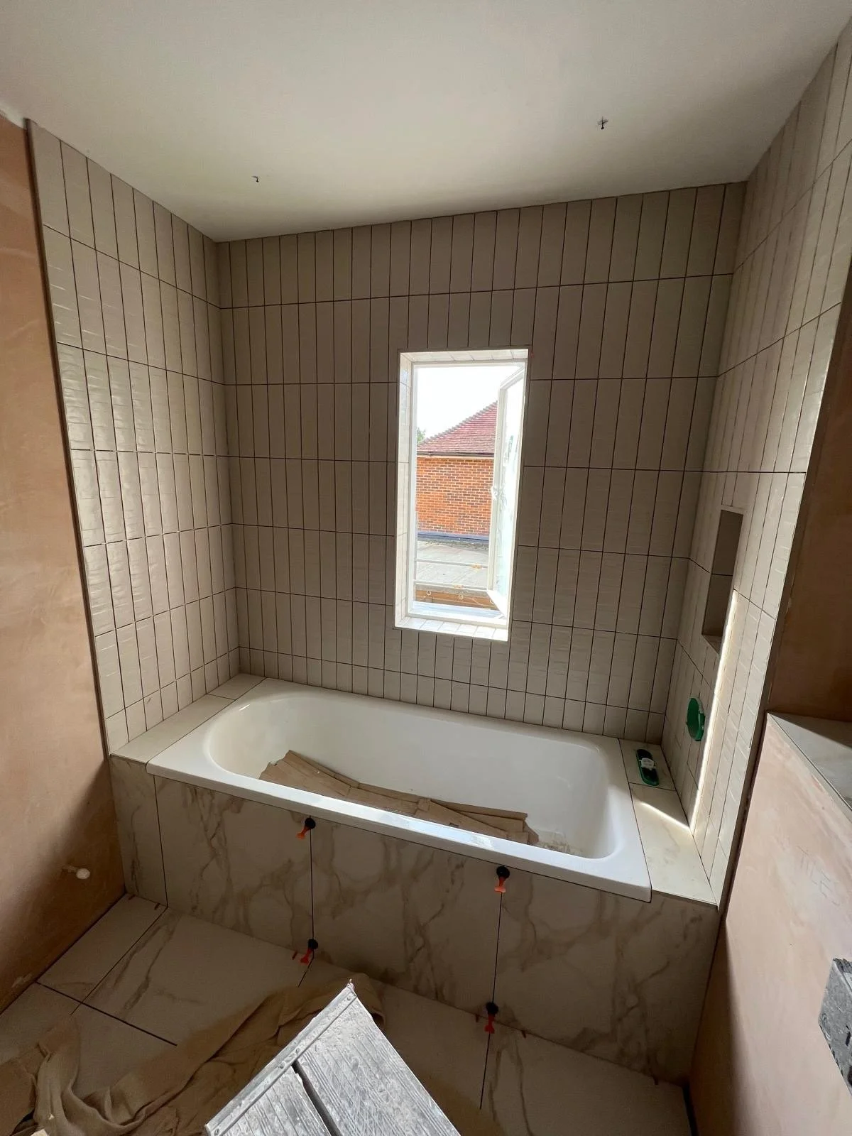 Bathroom under construction with a bathtub, tiled walls, and an open window.