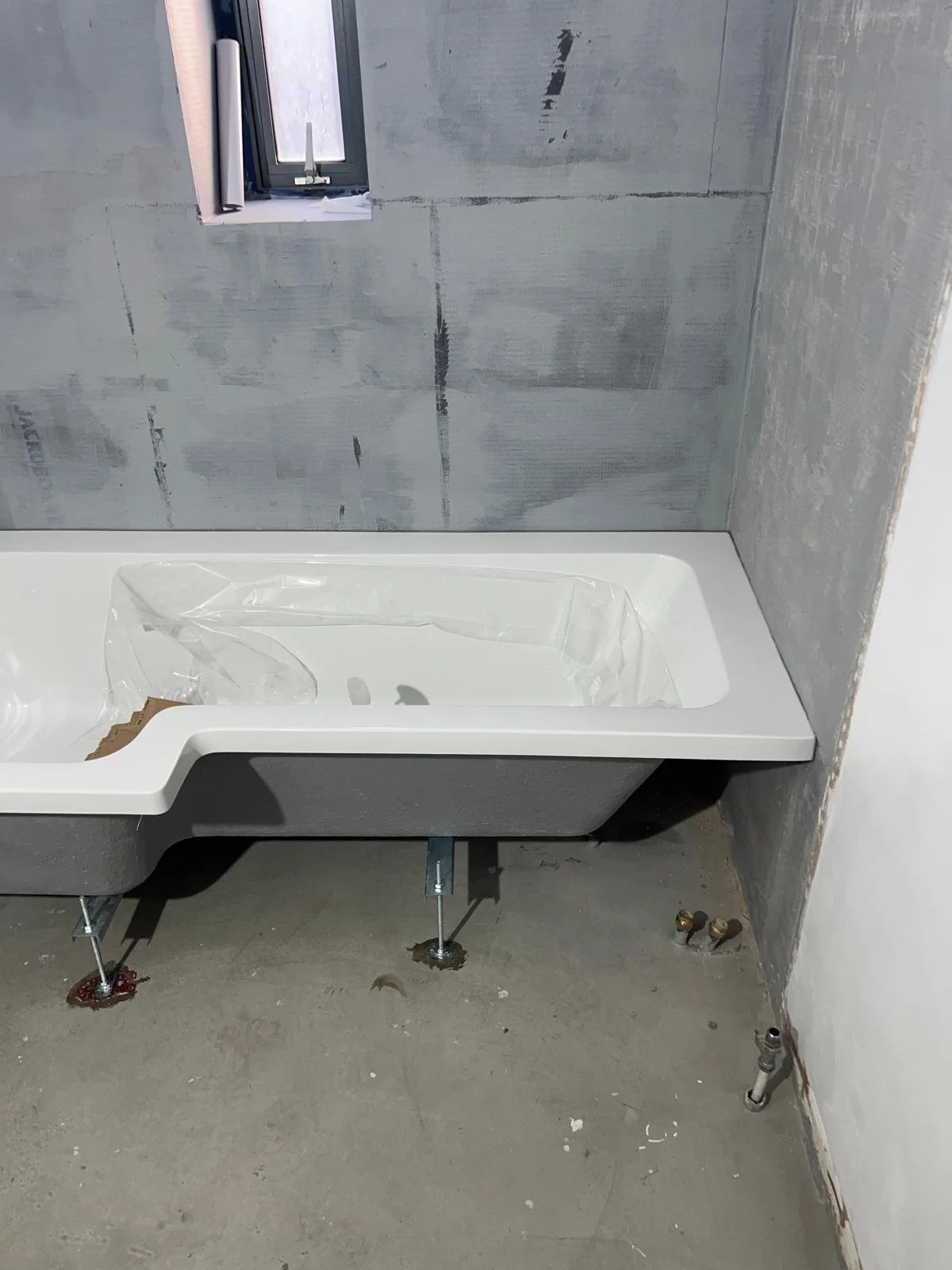 Bathroom under construction with vanity sink installed, a small window, and unfinished walls with exposed plumbing.