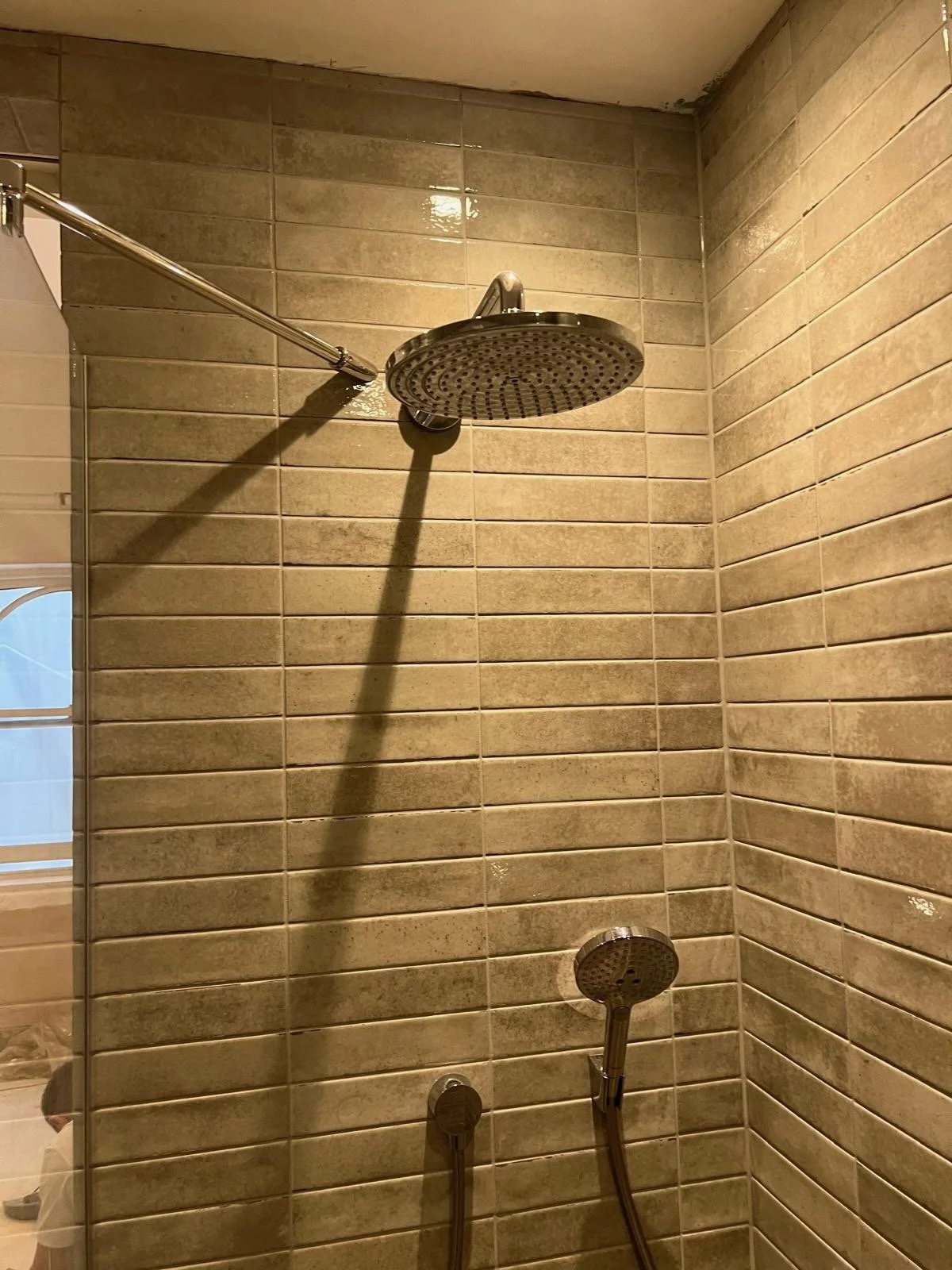 Shower with two showerheads, one fixed and one handheld, mounted on a tiled wall.