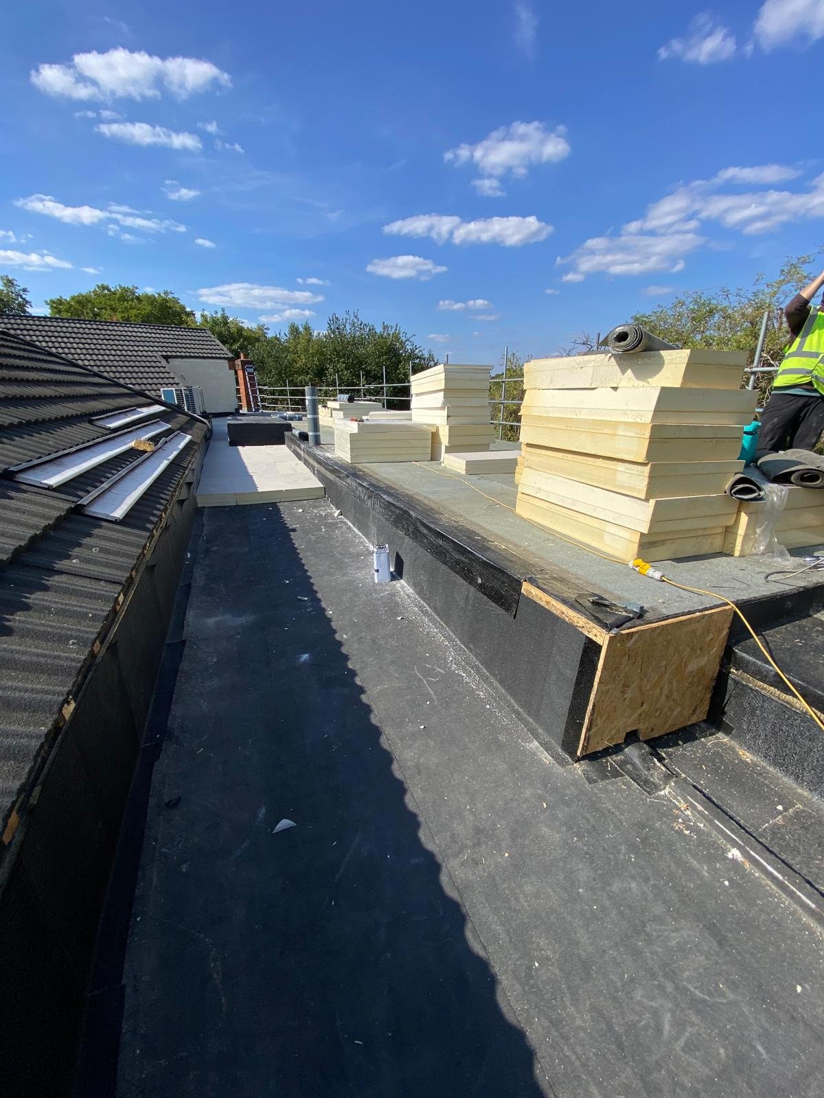 Construction site on a roof with piles of insulation foam boards and weatherproofing materials, clear blue sky in the background.